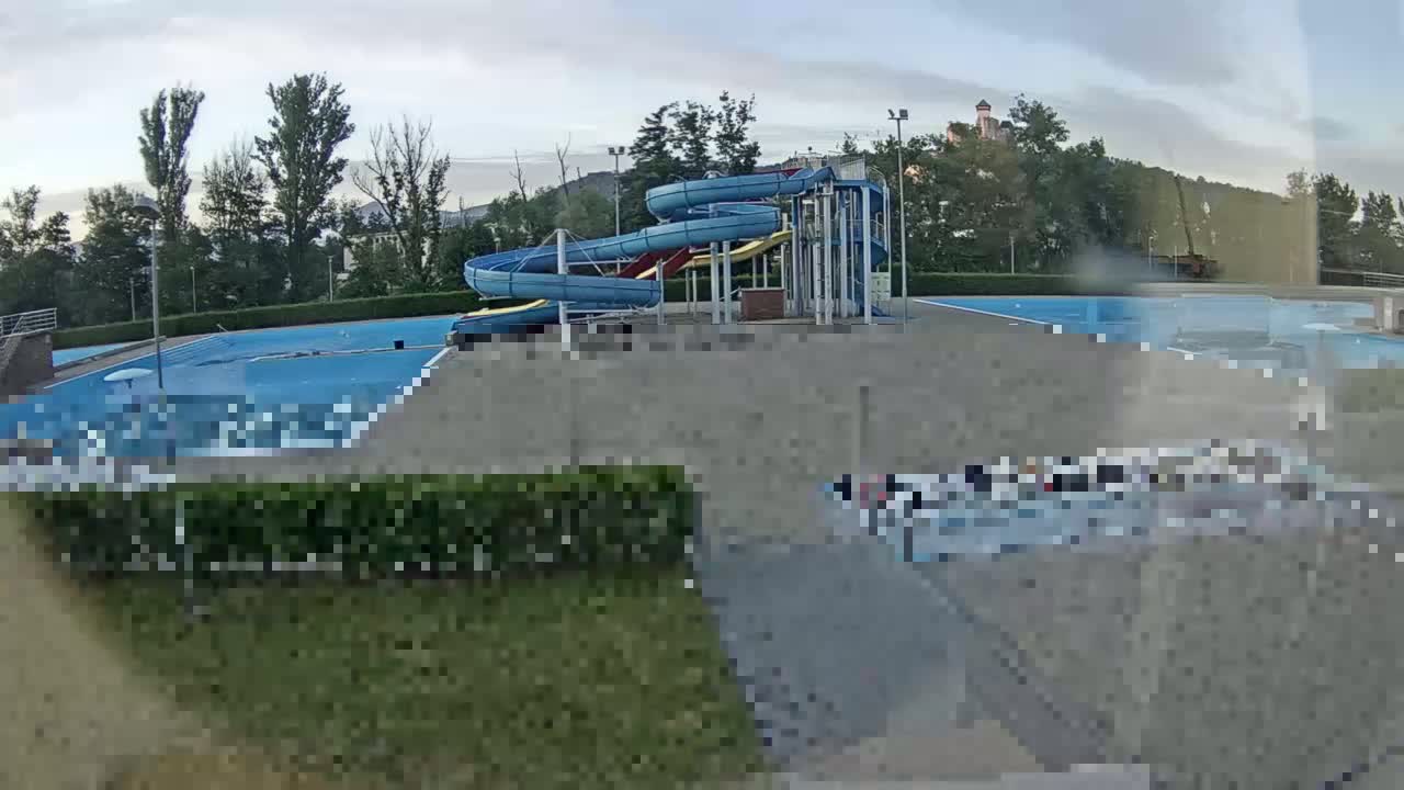 An outdoor swimming pool complex with multiple water slides is visible under a partly cloudy sky.