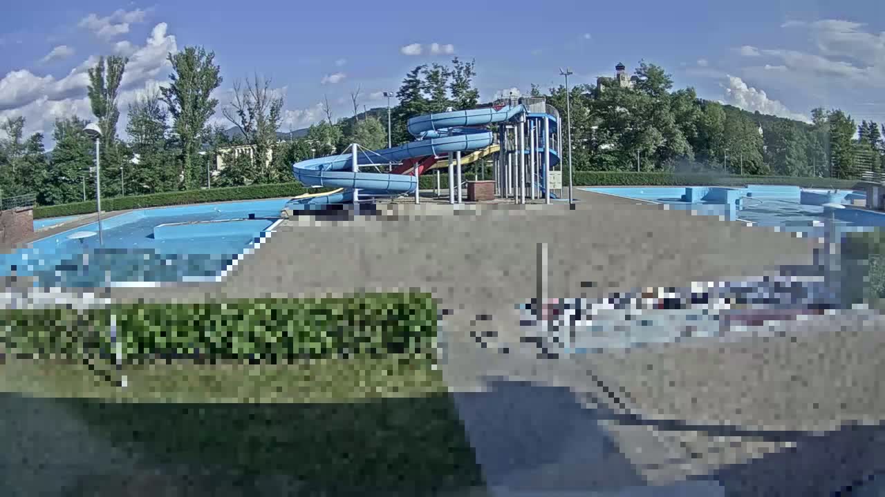 An outdoor swimming pool complex with multiple water slides is visible under a partly cloudy sky.