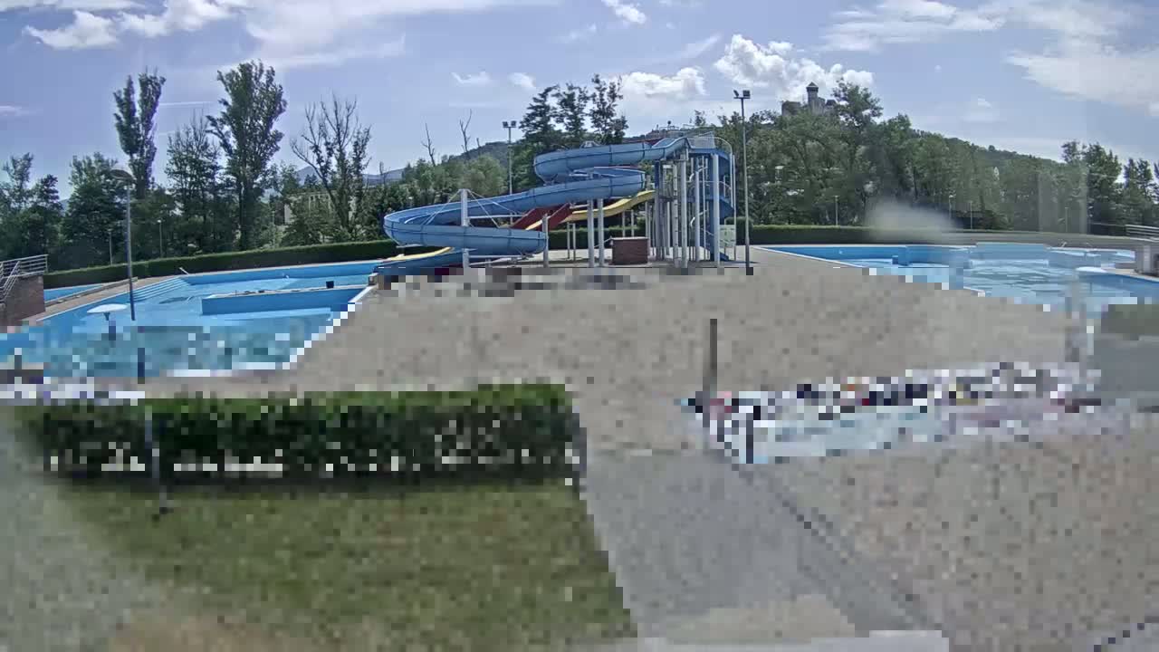 An outdoor swimming pool complex with water slides is visible under a partly cloudy sky.