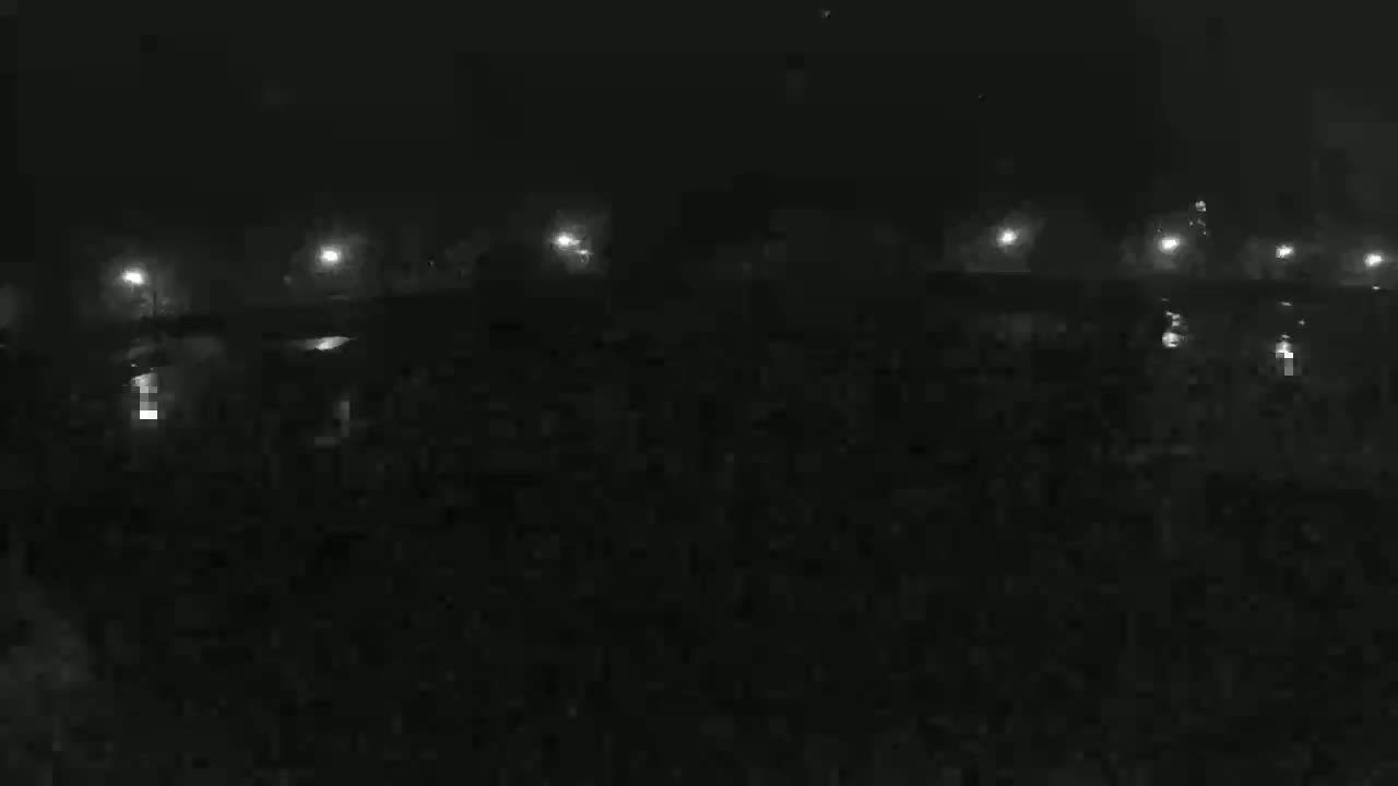 A nighttime, low-light view shows a dark, possibly watery area with faintly lit structures and lights in the distance.