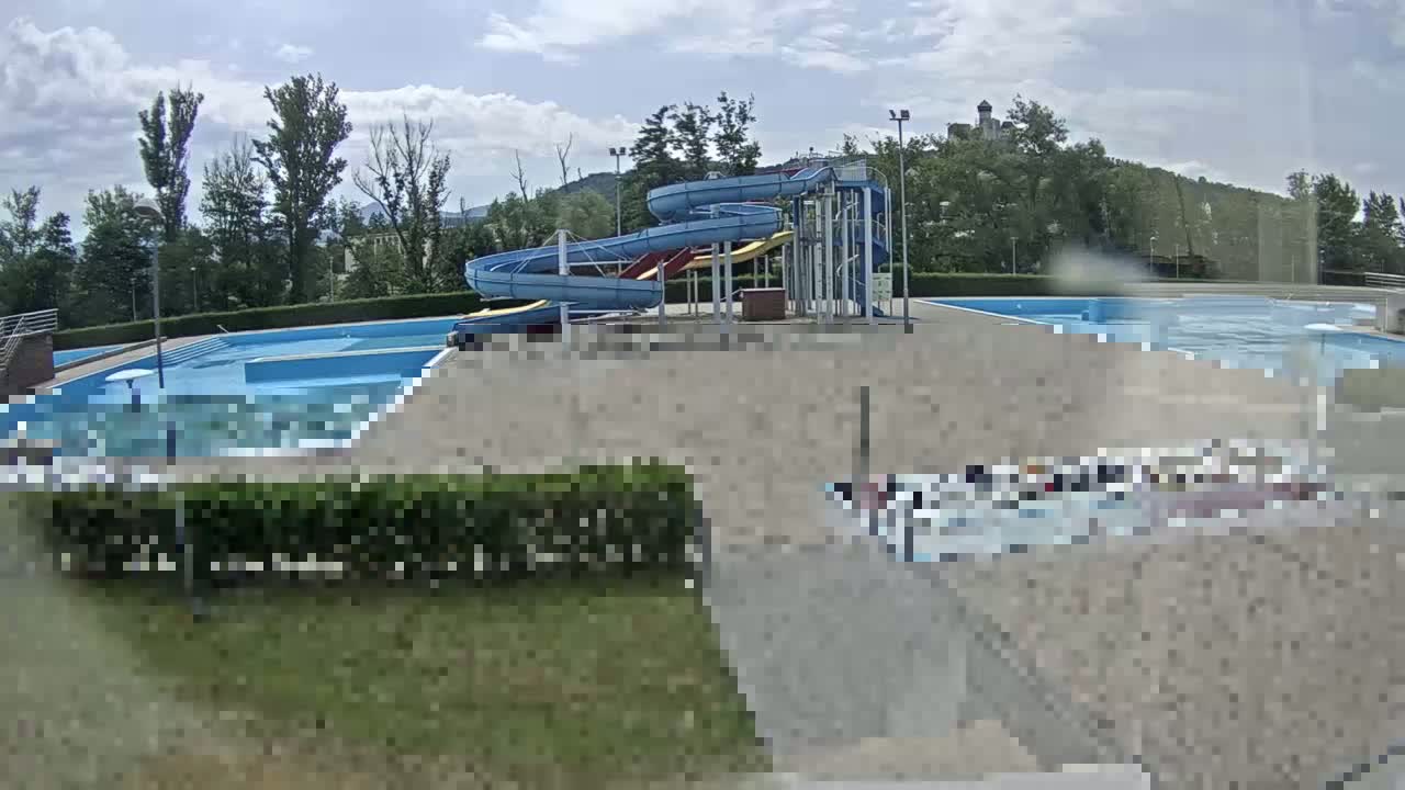 An outdoor swimming pool complex with water slides is visible under a partly cloudy sky.