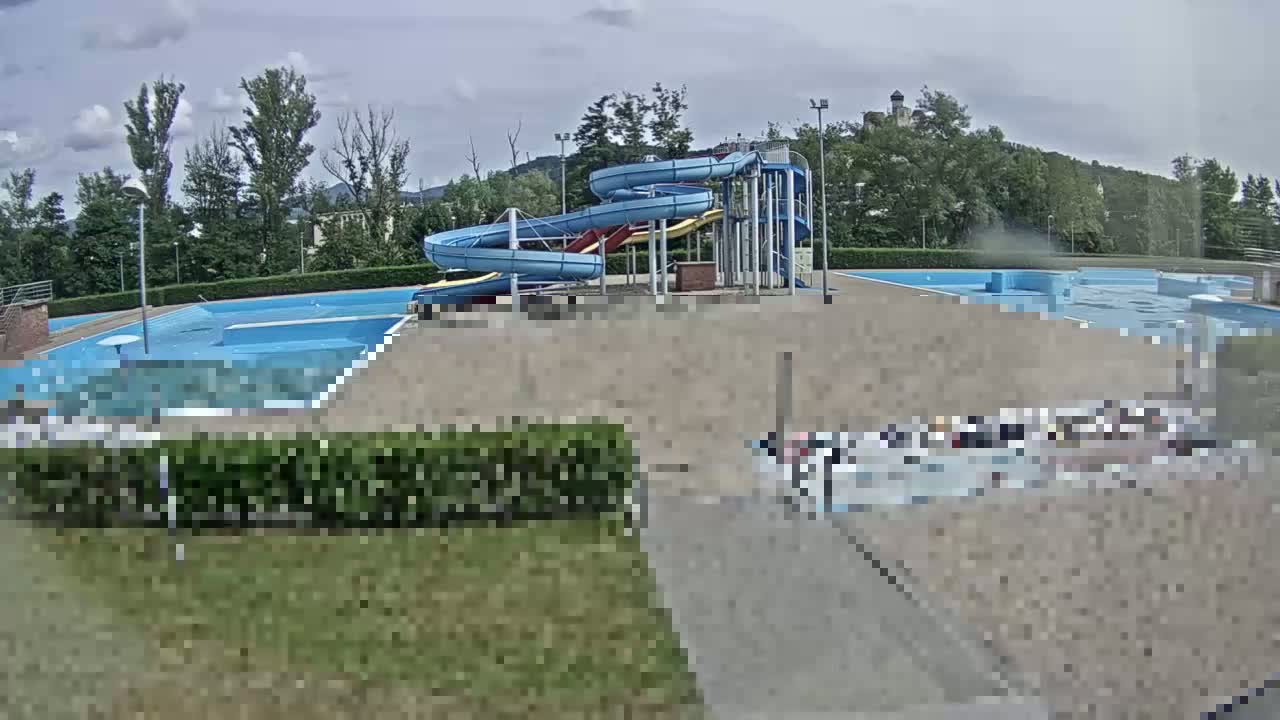 An outdoor swimming pool complex with two spiral water slides, under a partly cloudy sky.