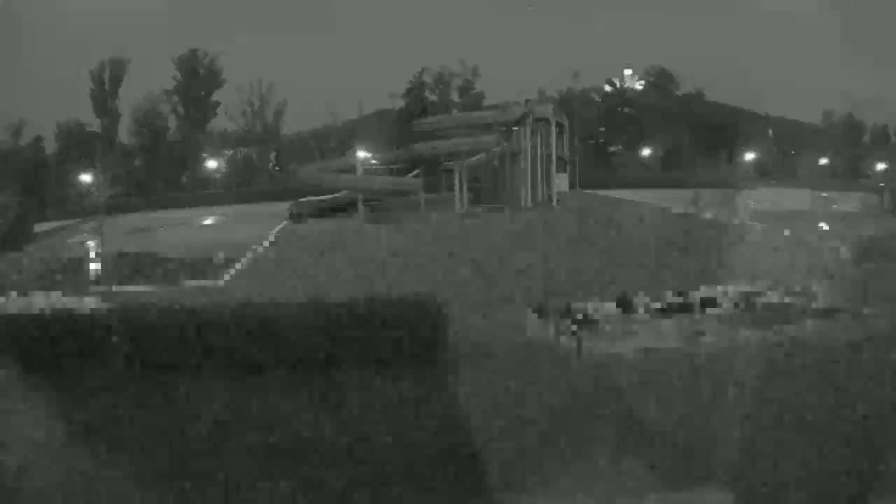 A nighttime, low-light view shows a large, indistinct structure near some trees and sparsely lit landscaping.