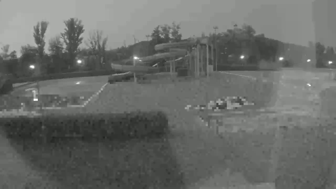 A nighttime, low-light view shows water slides in a mostly empty parking lot with trees and some lights in the background.