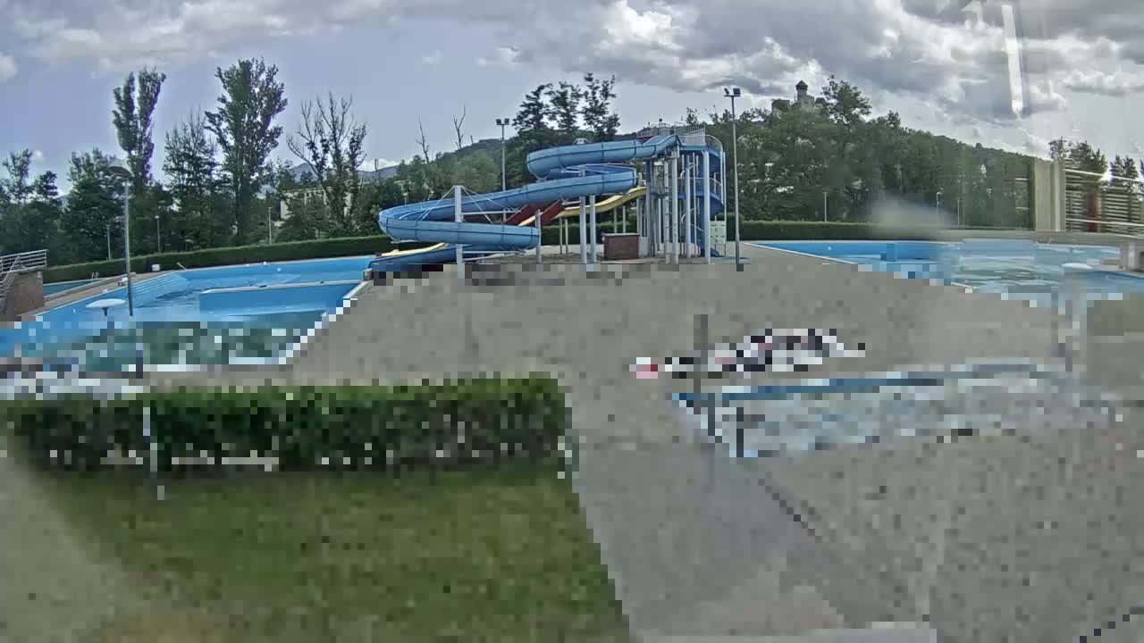 An outdoor swimming pool complex with two spiral water slides is visible under a partly cloudy sky.