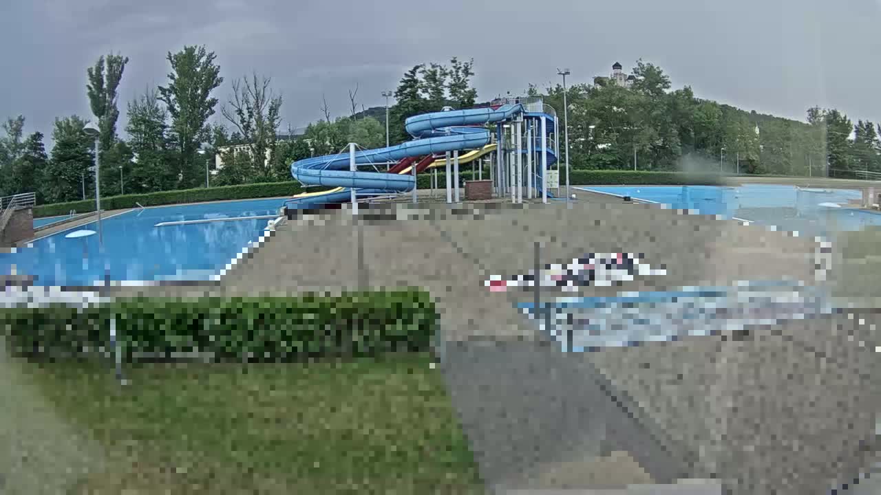 An outdoor swimming pool complex with two water slides is seen on an overcast day.