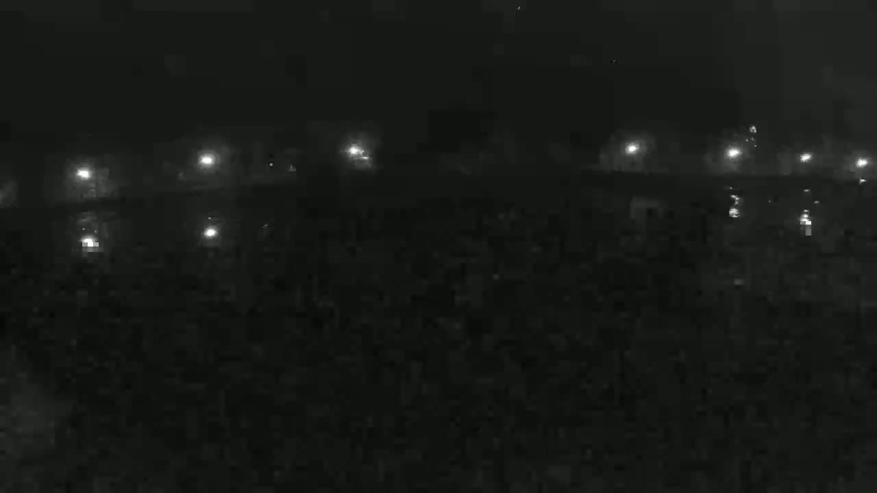 A nighttime, foggy view shows a dark expanse of ground with a row of lights in the distance, appearing to be a structure illuminated faintly.