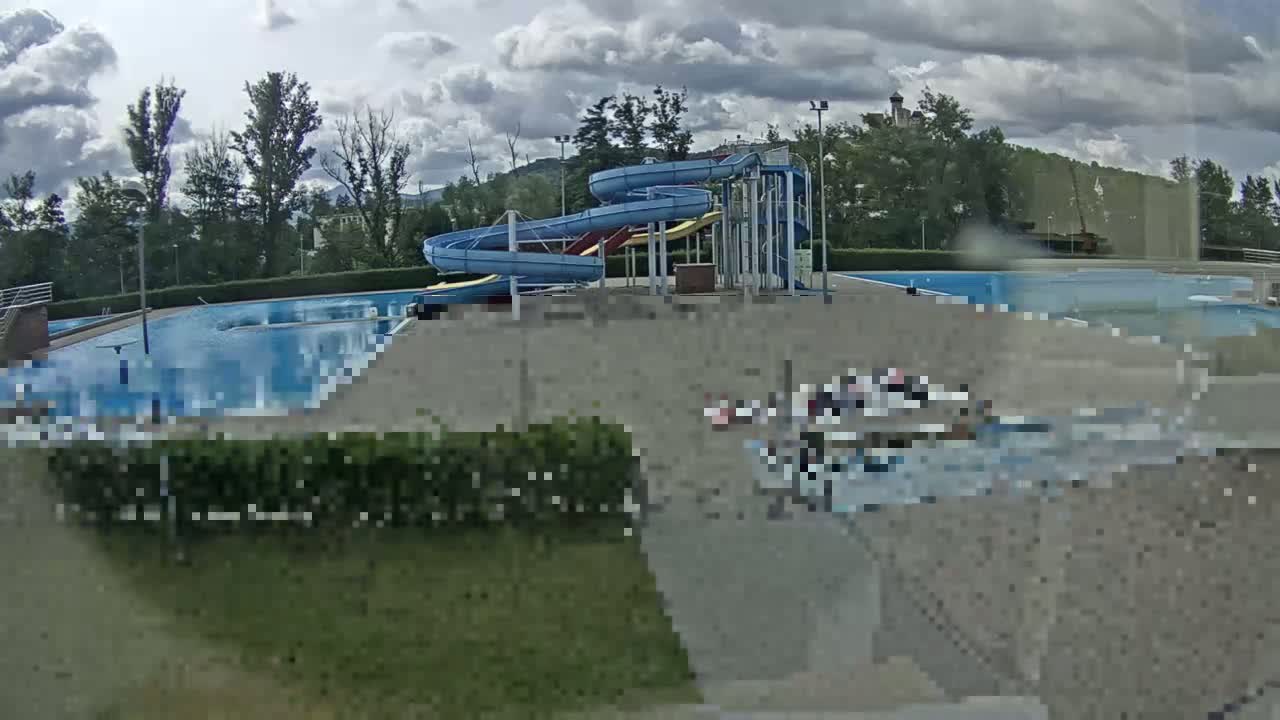An outdoor swimming pool complex with water slides is visible under a partly cloudy sky.