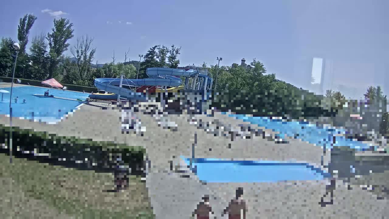 An outdoor water park with several pools and water slides is populated by many people on a sunny day.