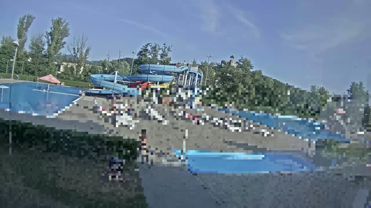 A sunny outdoor water park with multiple pools, water slides, and many people relaxing and swimming.