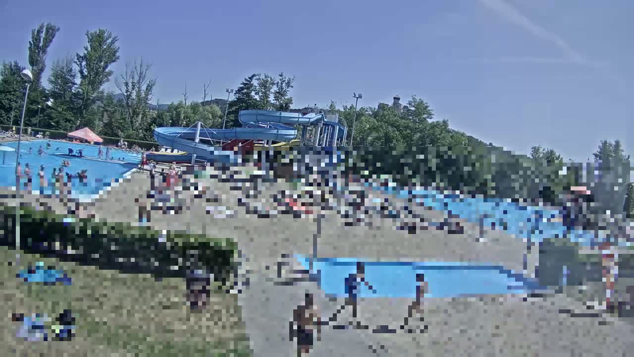 A sunny day at a water park shows multiple pools with many people swimming and sunbathing around water slides.