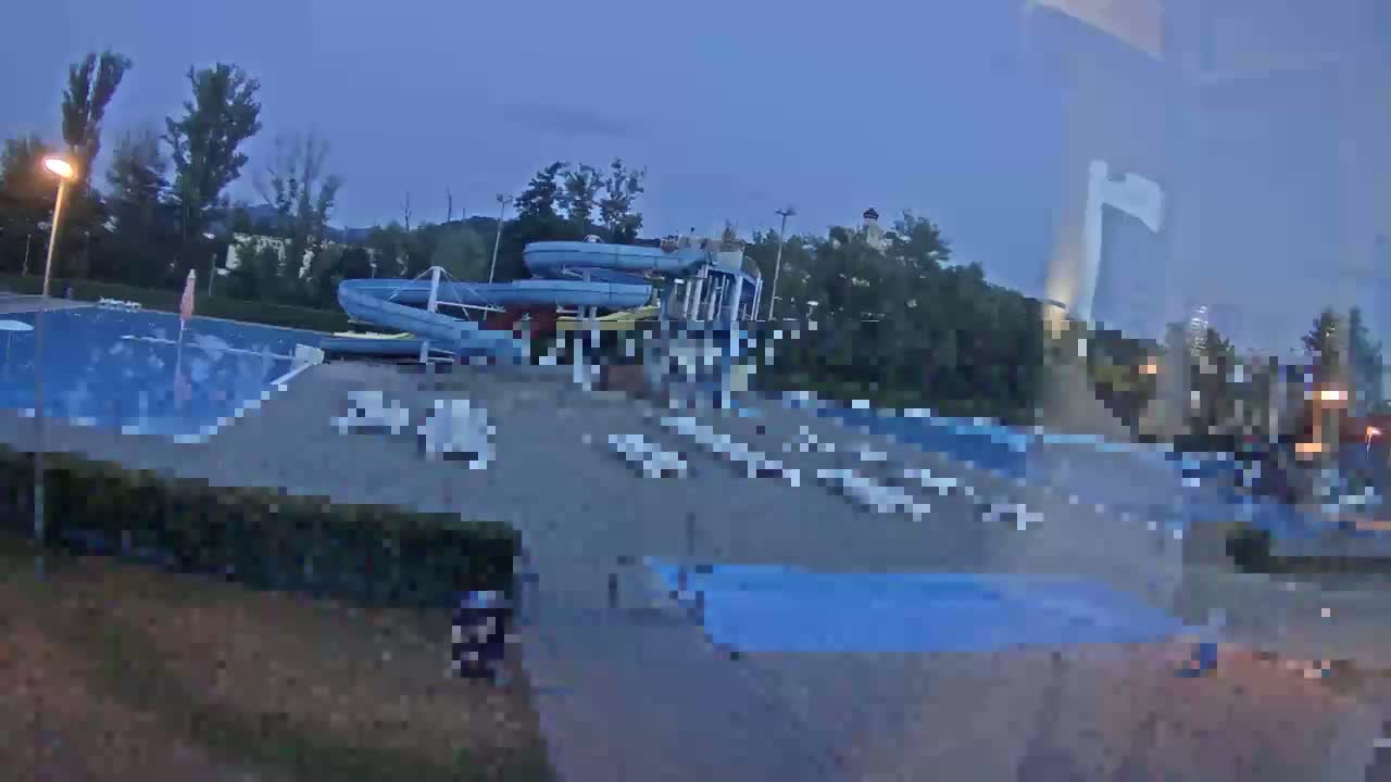 An outdoor swimming pool area with water slides is mostly empty at dusk.