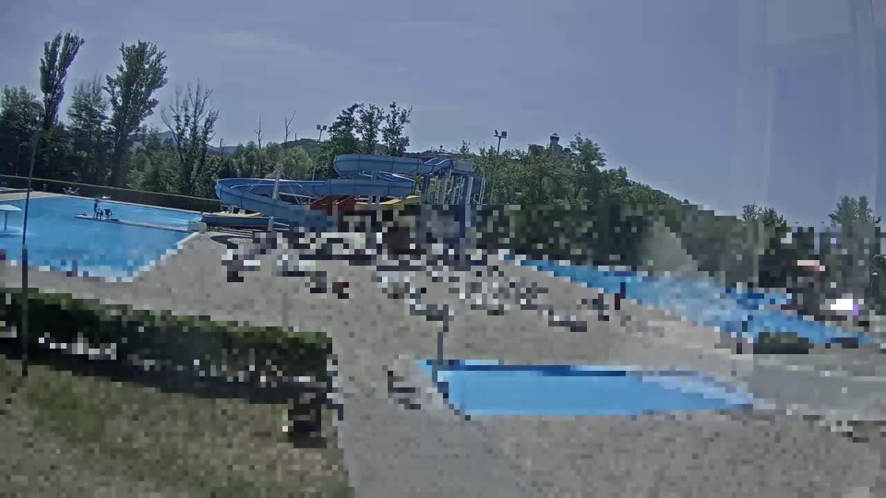 An outdoor swimming pool area with water slides is mostly empty at dusk.