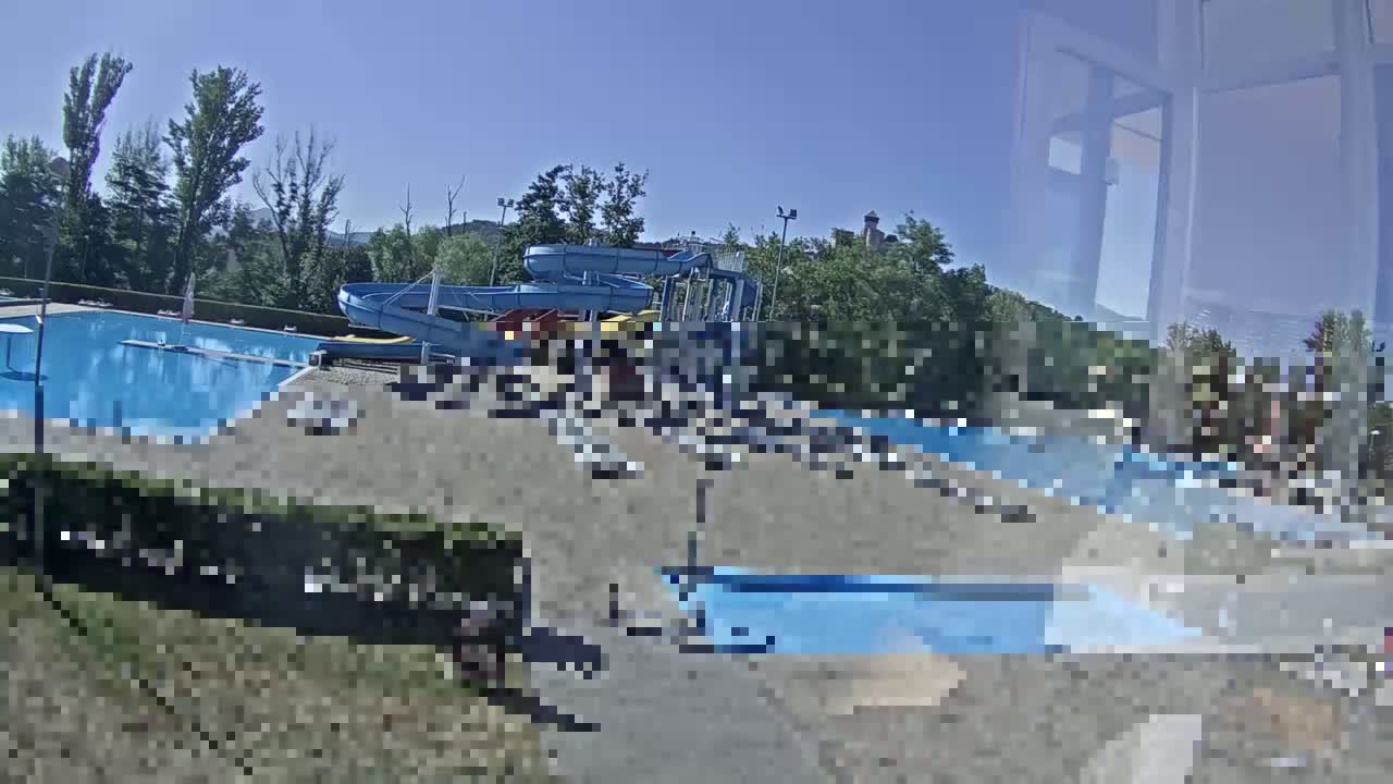 A sunny outdoor water park with several pools and water slides surrounded by trees.