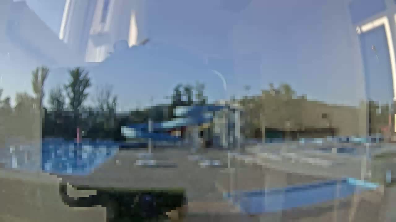A view through a window shows an outdoor water park with multiple swimming pools under a cloudy sky.
