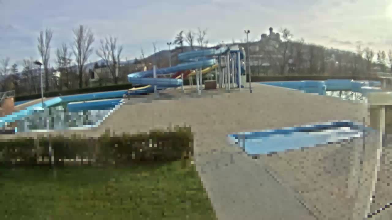 A blurry view through a window shows a swimming pool and surrounding area on a sunny day.