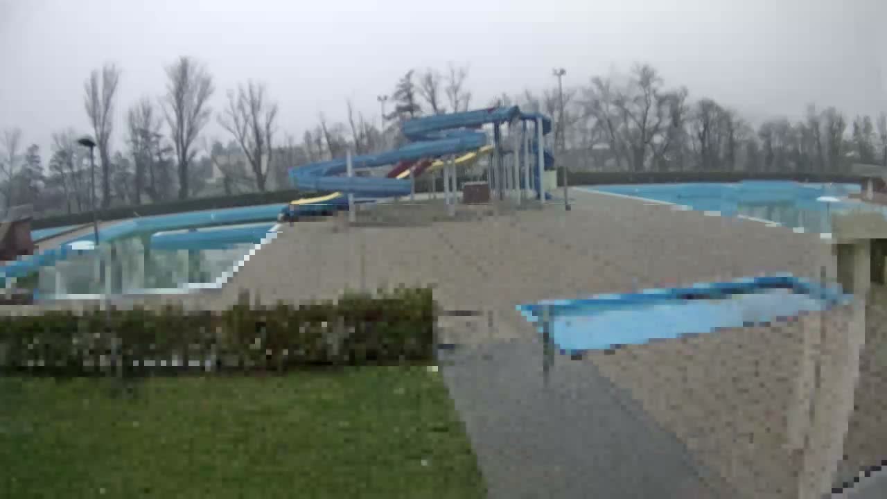 An empty outdoor water park featuring a large blue spiral waterslide and multiple pools sits under a grey, overcast sky, surrounded by bare trees.