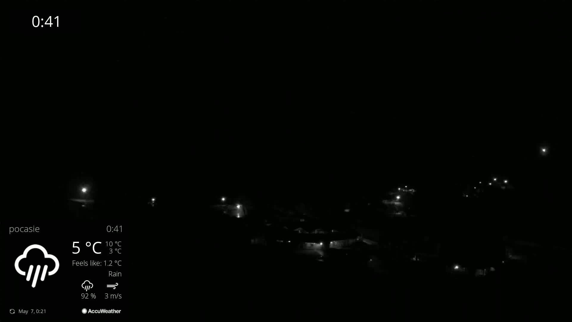 A nighttime, rainy view of dimly lit houses and streets, with a dark sky.