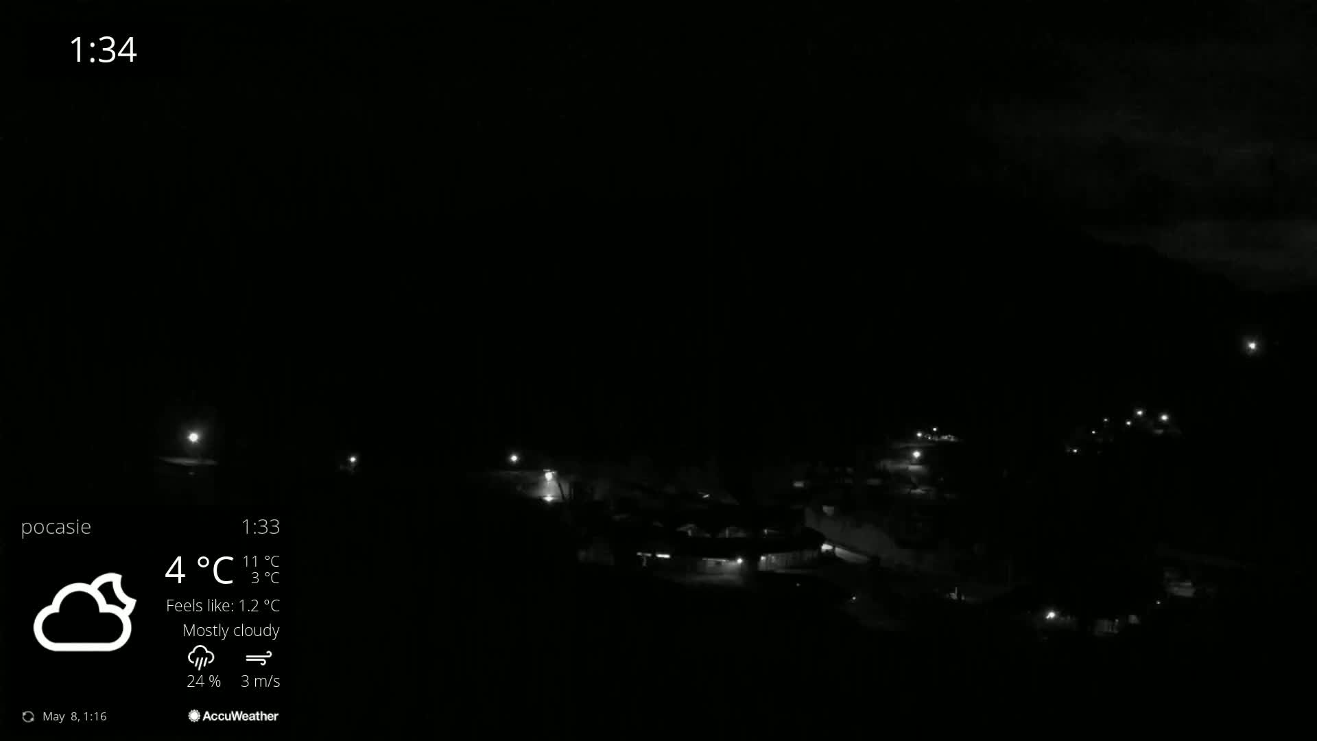 A nighttime, mostly cloudy view of a small town with scattered lights visible under a dark sky.