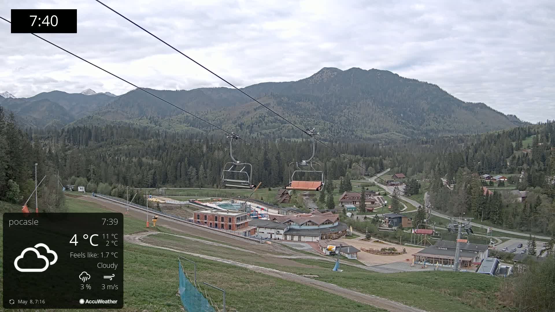 A ski resort under cloudy skies, with a chairlift and buildings nestled in a valley surrounded by mountains.