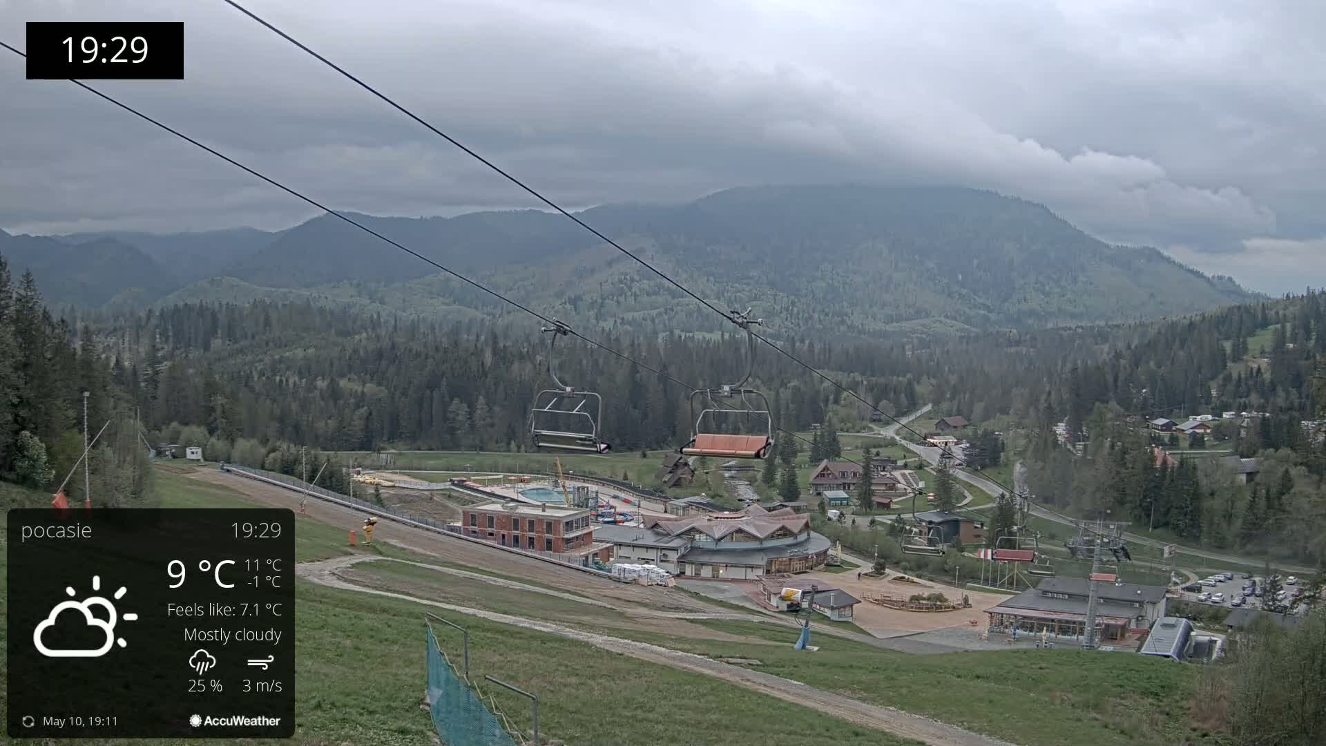 A mostly cloudy mountain scene with a chairlift and buildings below, under a cool breeze.