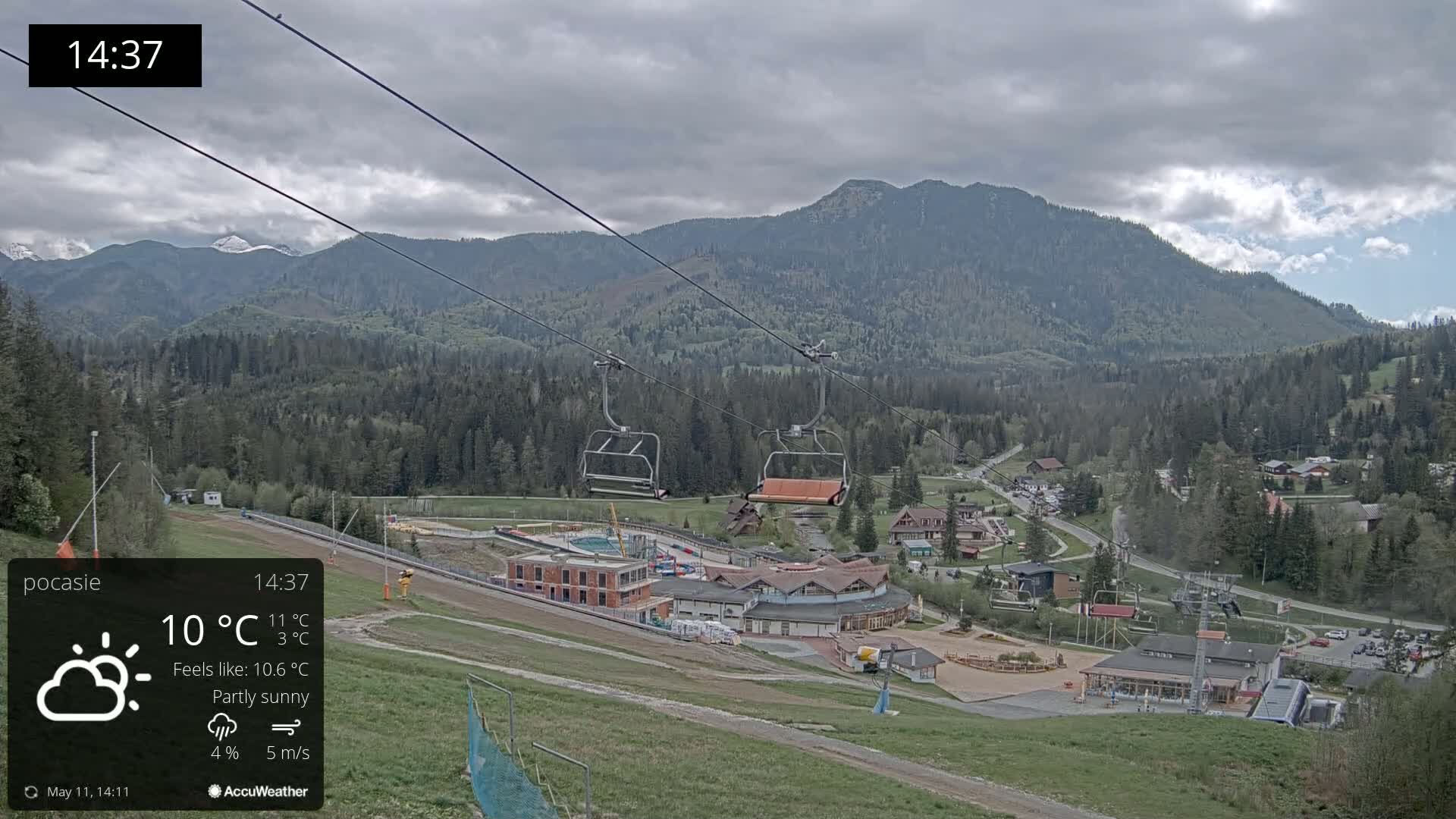 A partly sunny mountain scene with a chairlift and buildings below, under overcast skies.