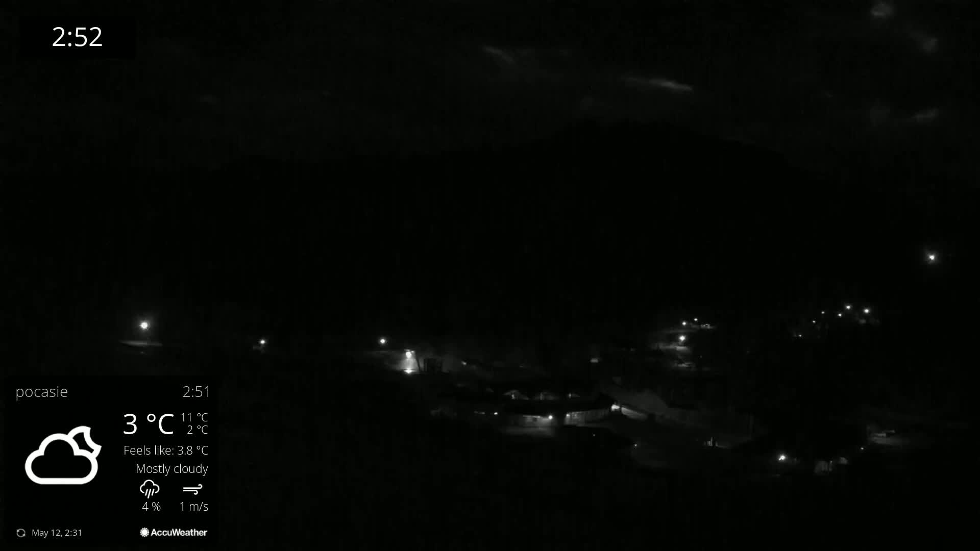 A mostly cloudy night scene shows dimly lit buildings and faint lights scattered across a dark landscape.