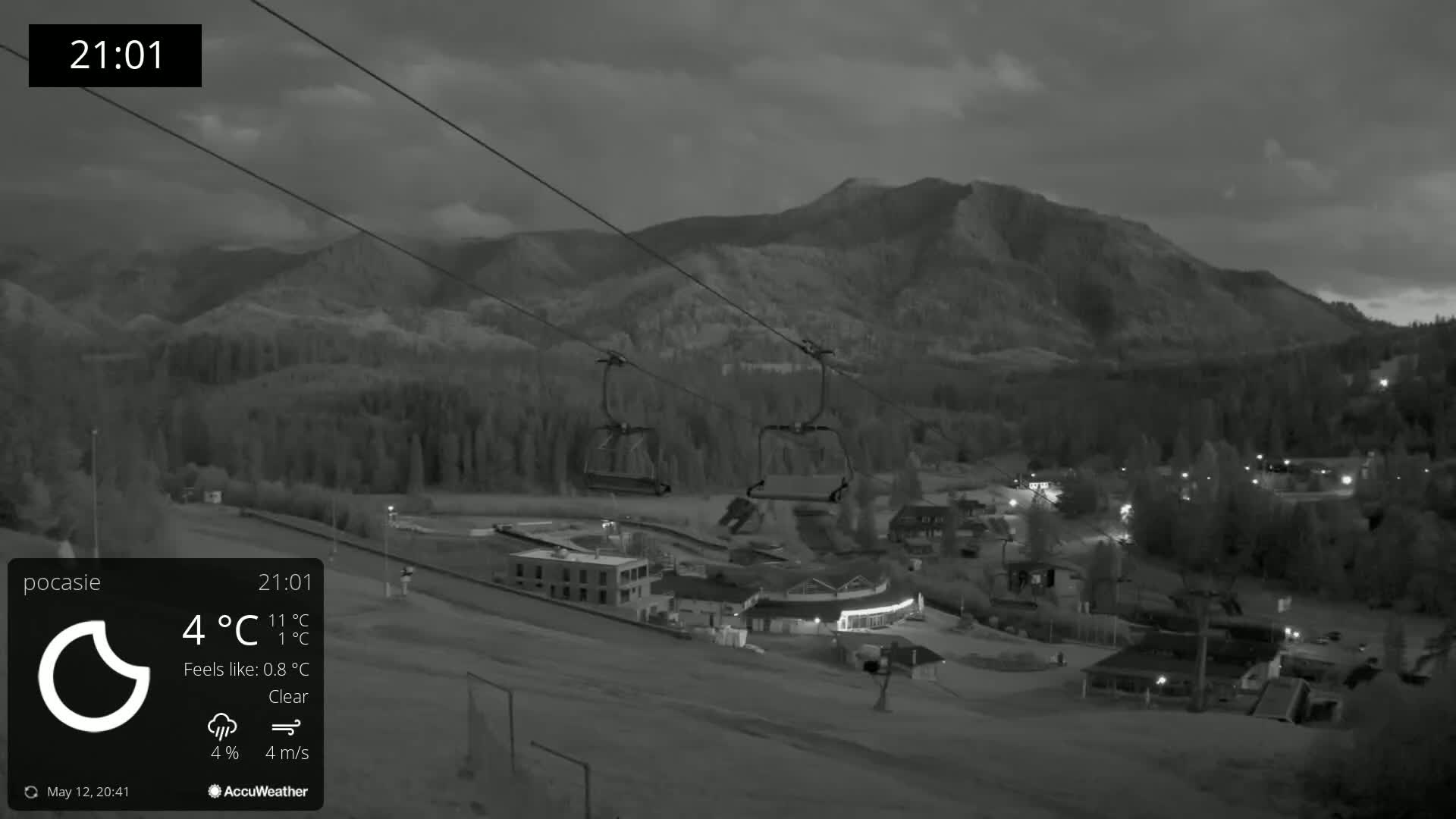 A nighttime, clear view of a ski resort with chairlifts and a mountain in the background, under a partly cloudy sky.