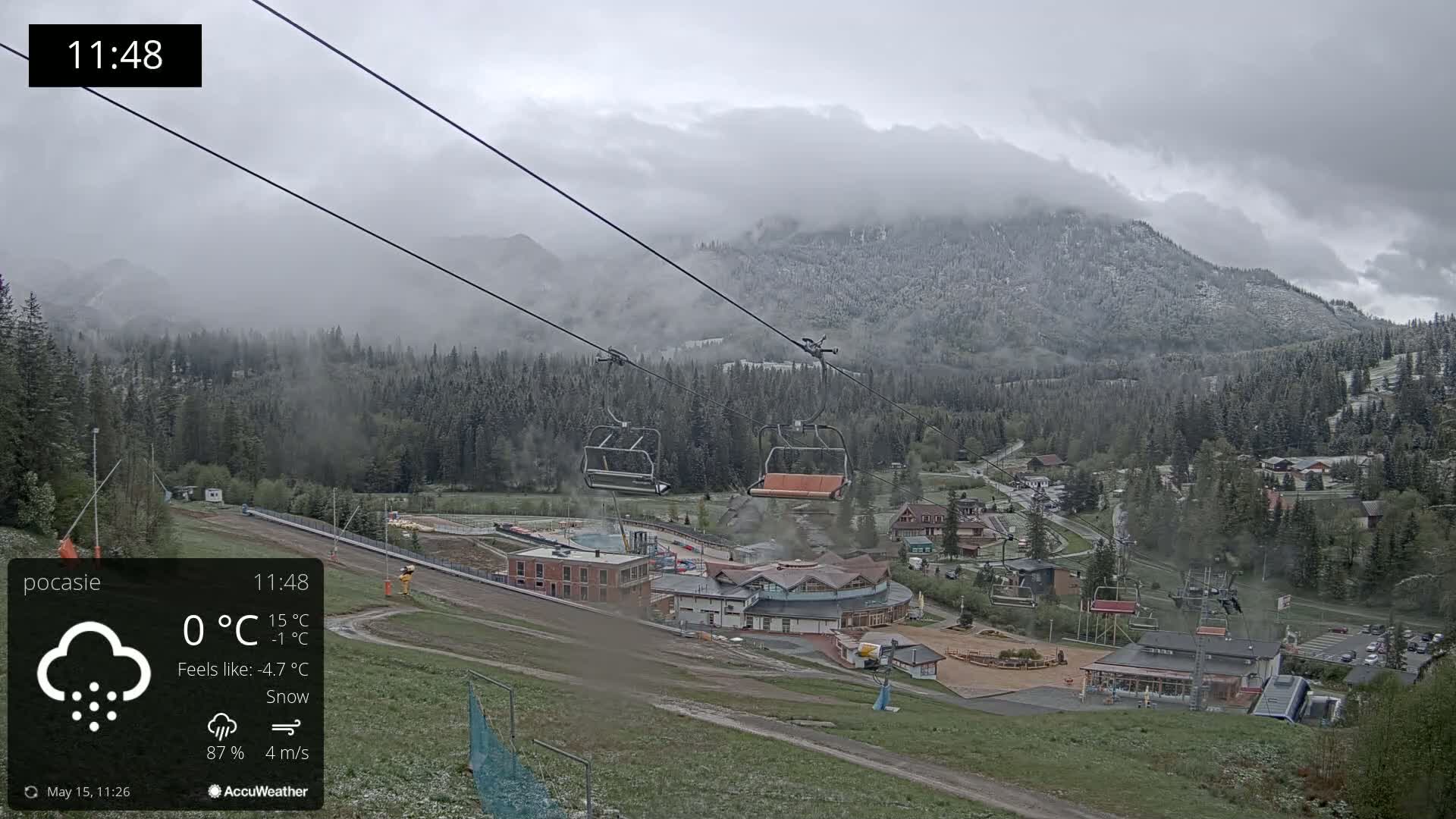 A chairlift ascends a snowy mountainside overlooking a village under a cloudy, snowy sky.