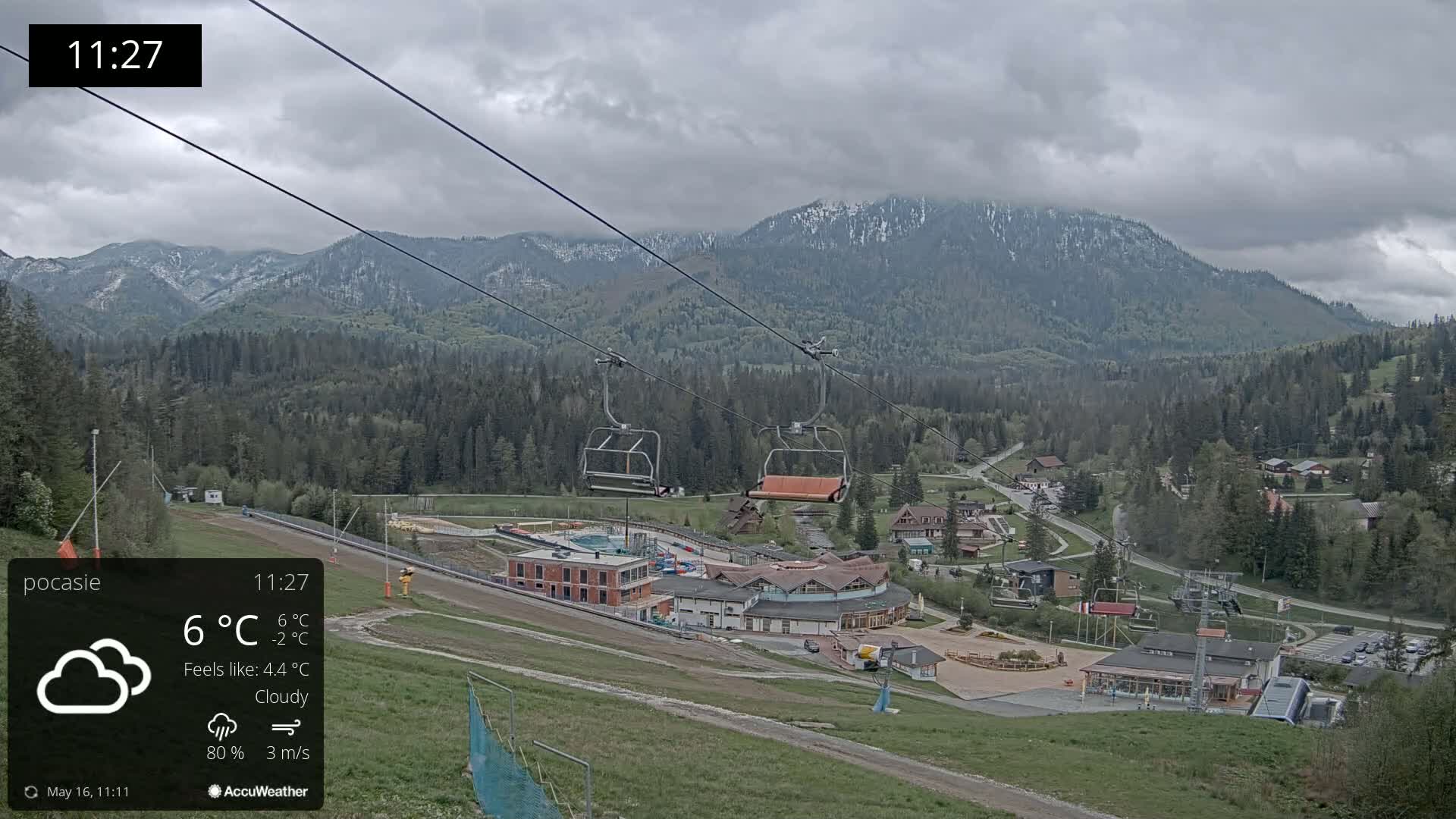 A cloudy view of a ski resort nestled in a valley between snow-capped mountains, with chairlifts visible and a light breeze.