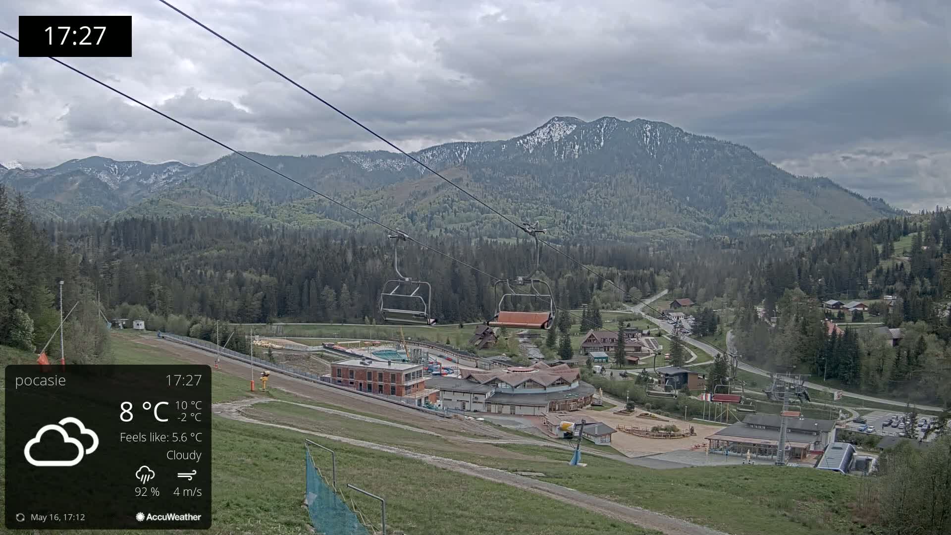 A cloudy mountain vista shows a ski resort with a chairlift and buildings below a snow-capped mountain range.