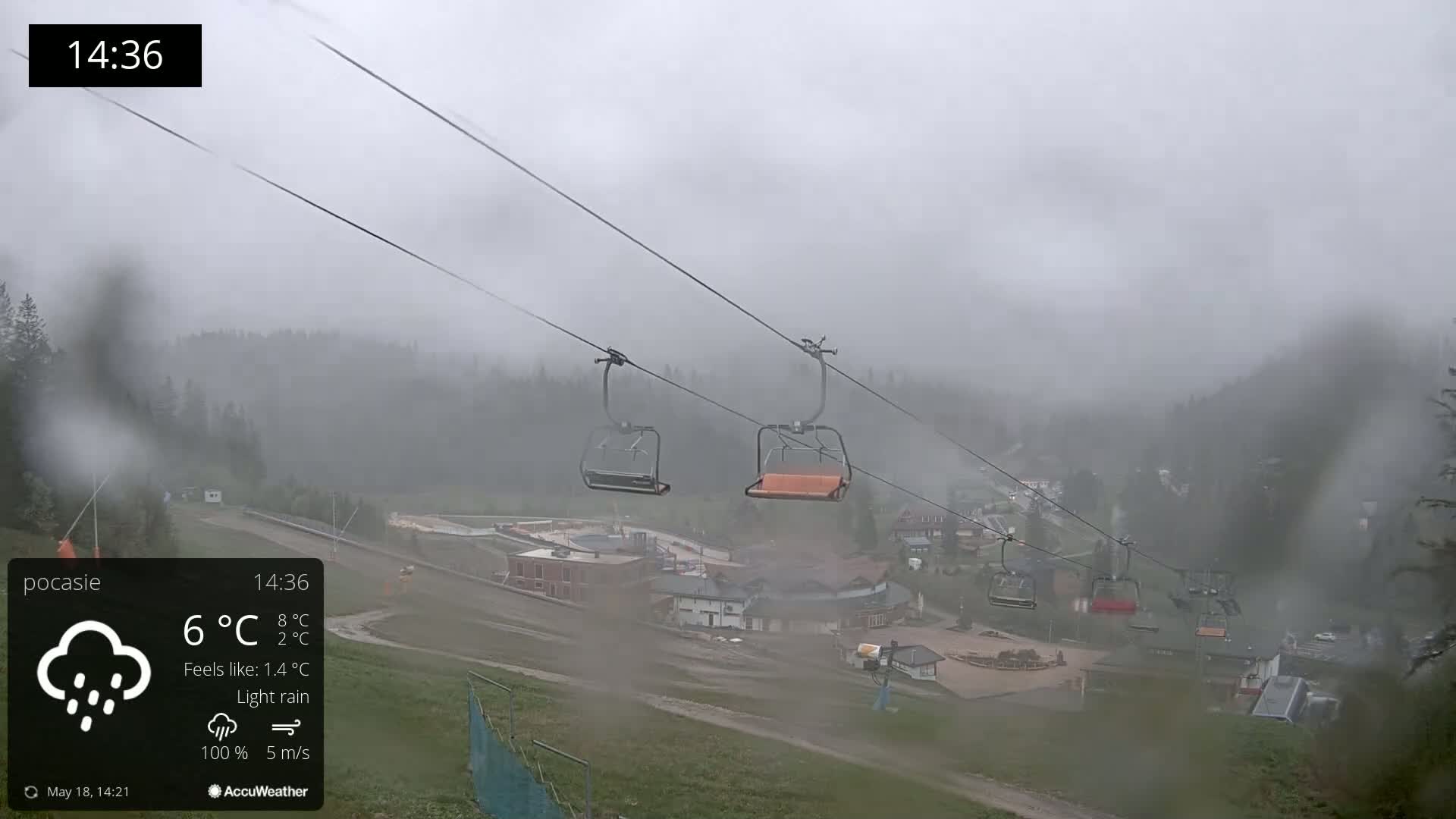 A foggy, rainy mountain scene shows empty chairlifts above a village and forested hillsides.