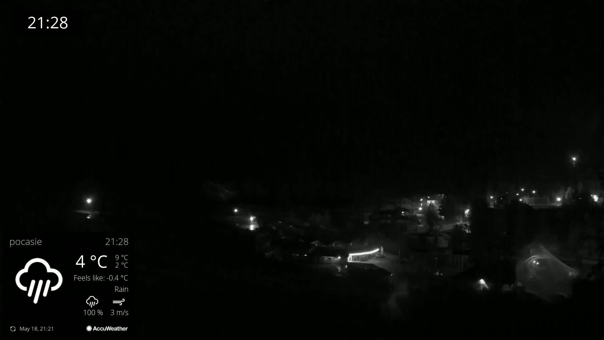 A nighttime, rainy view of a dimly lit town with scattered streetlights.