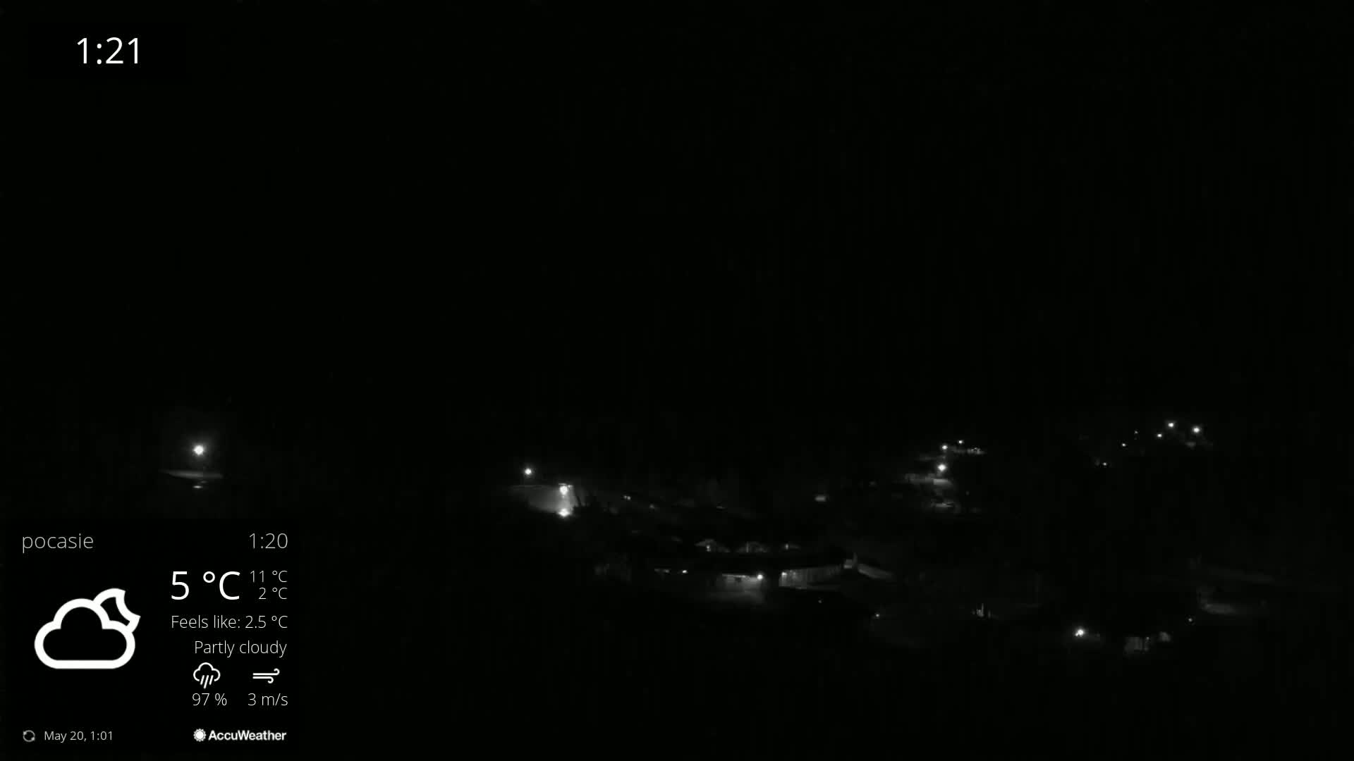 A nighttime, partly cloudy scene shows a small settlement with faint lights visible under a dark sky.