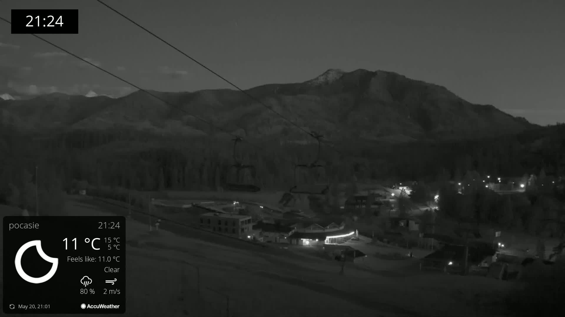 A nighttime, clear view of a ski resort with a mountain in the background, illuminated by lights, and a chairlift visible under a dark sky.