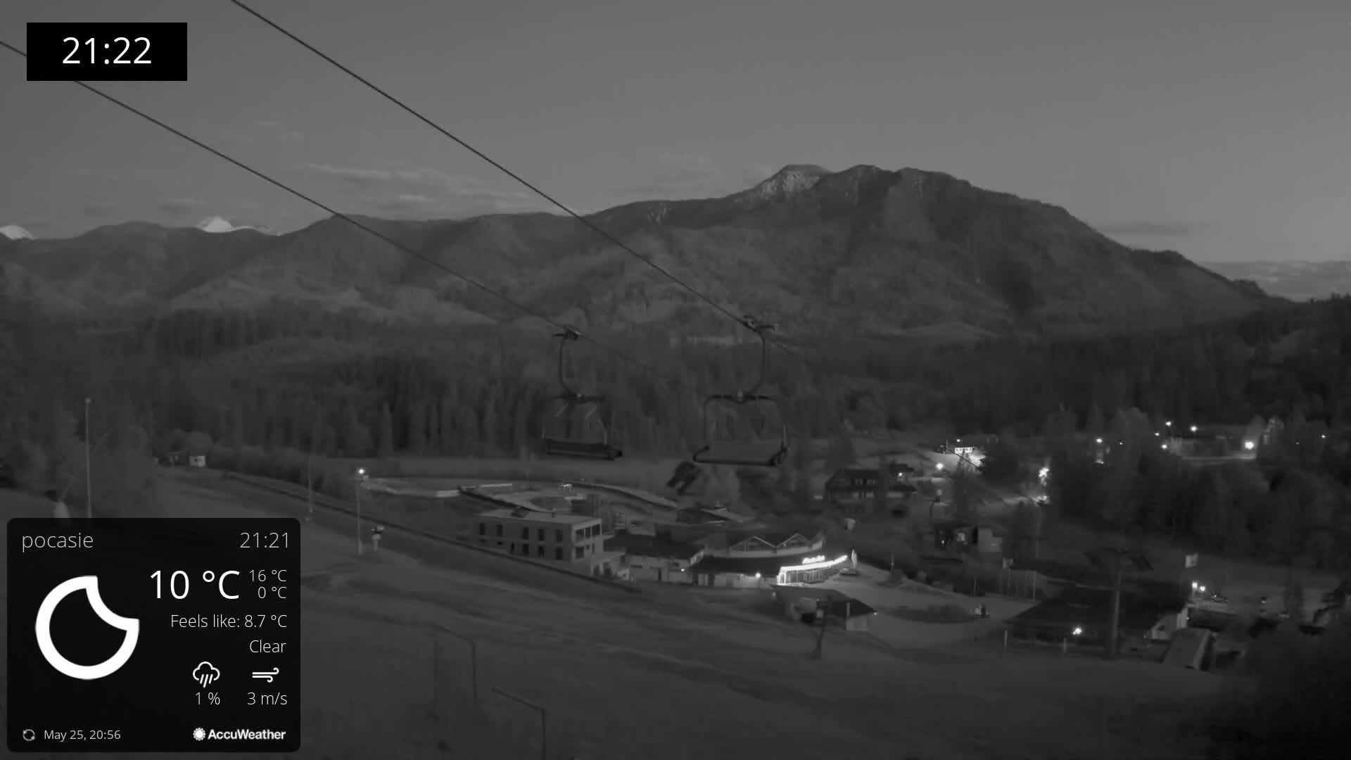 A nighttime, clear view of a ski lift and resort below a mountain range under a twilight sky.