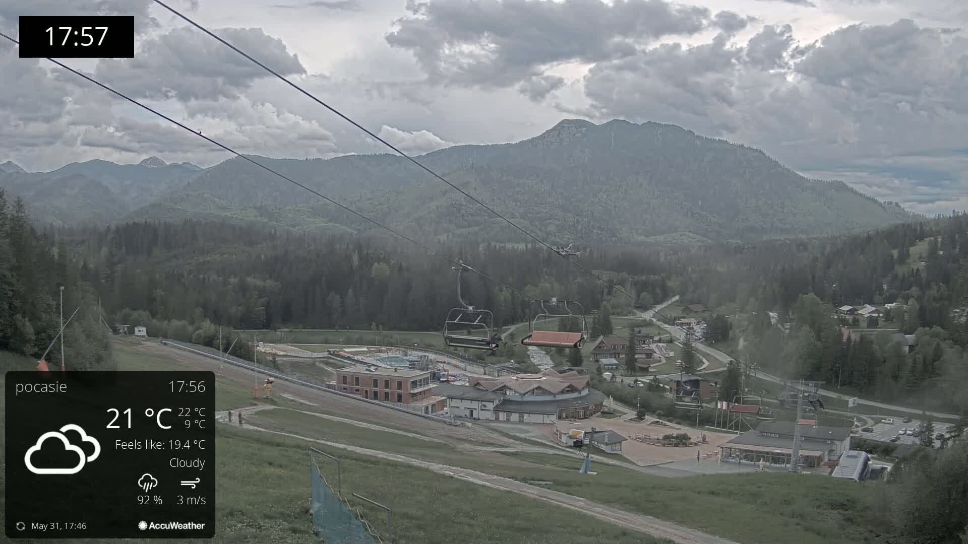 A cloudy view of a mountain resort with a chairlift, buildings, and green hills under a gray sky.
