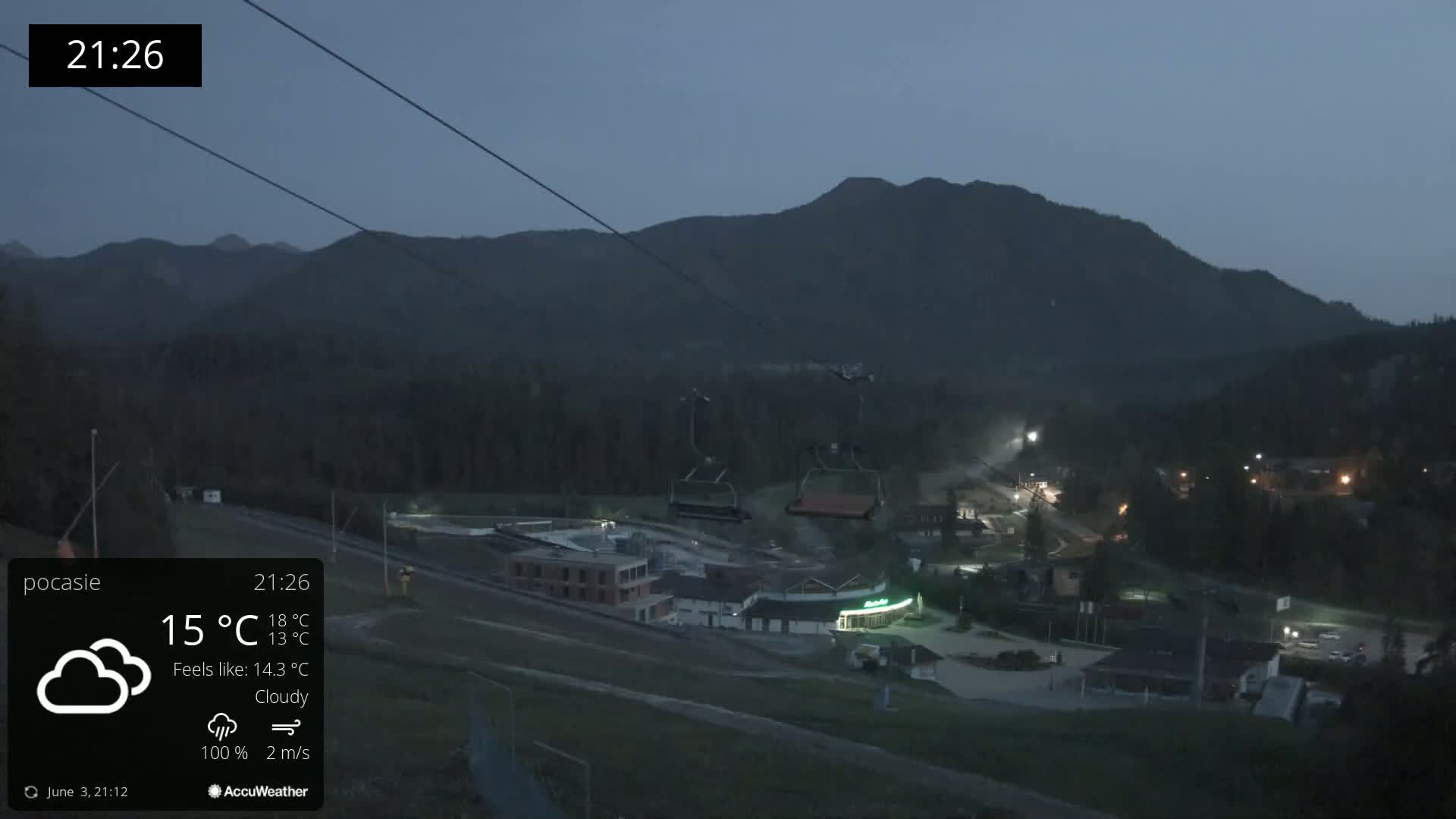 A nighttime, cloudy view of a ski resort with a chairlift in the foreground and mountains in the background.