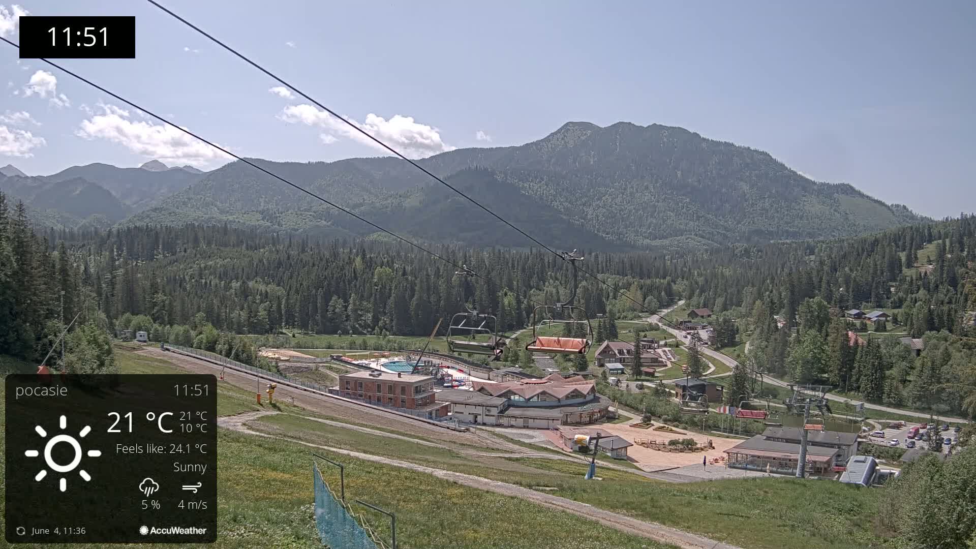 A sunny mountain resort with a chairlift and buildings is visible, with a mountain range in the background.