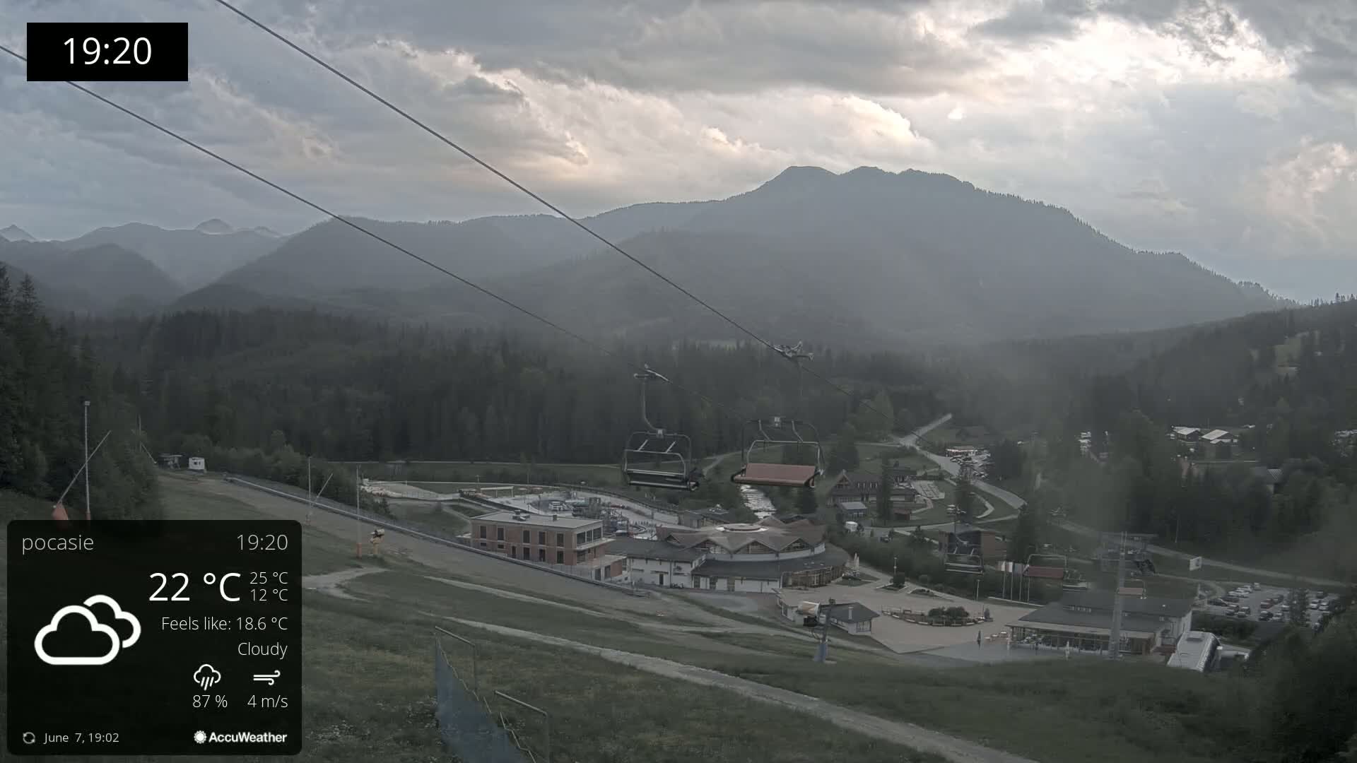 A cloudy, overcast view of a ski resort in the mountains at dusk, with a chairlift visible in the foreground.