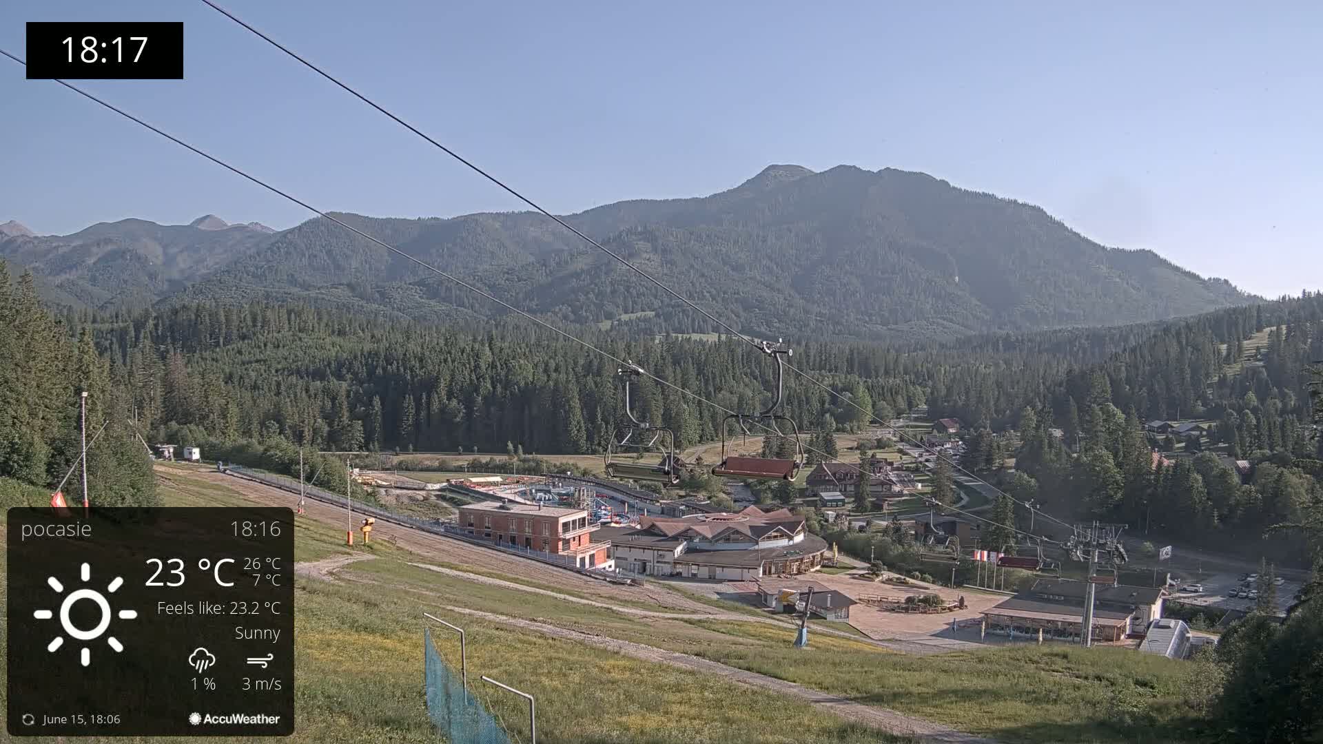 A sunny mountain valley scene with a chairlift and buildings, under a clear sky.