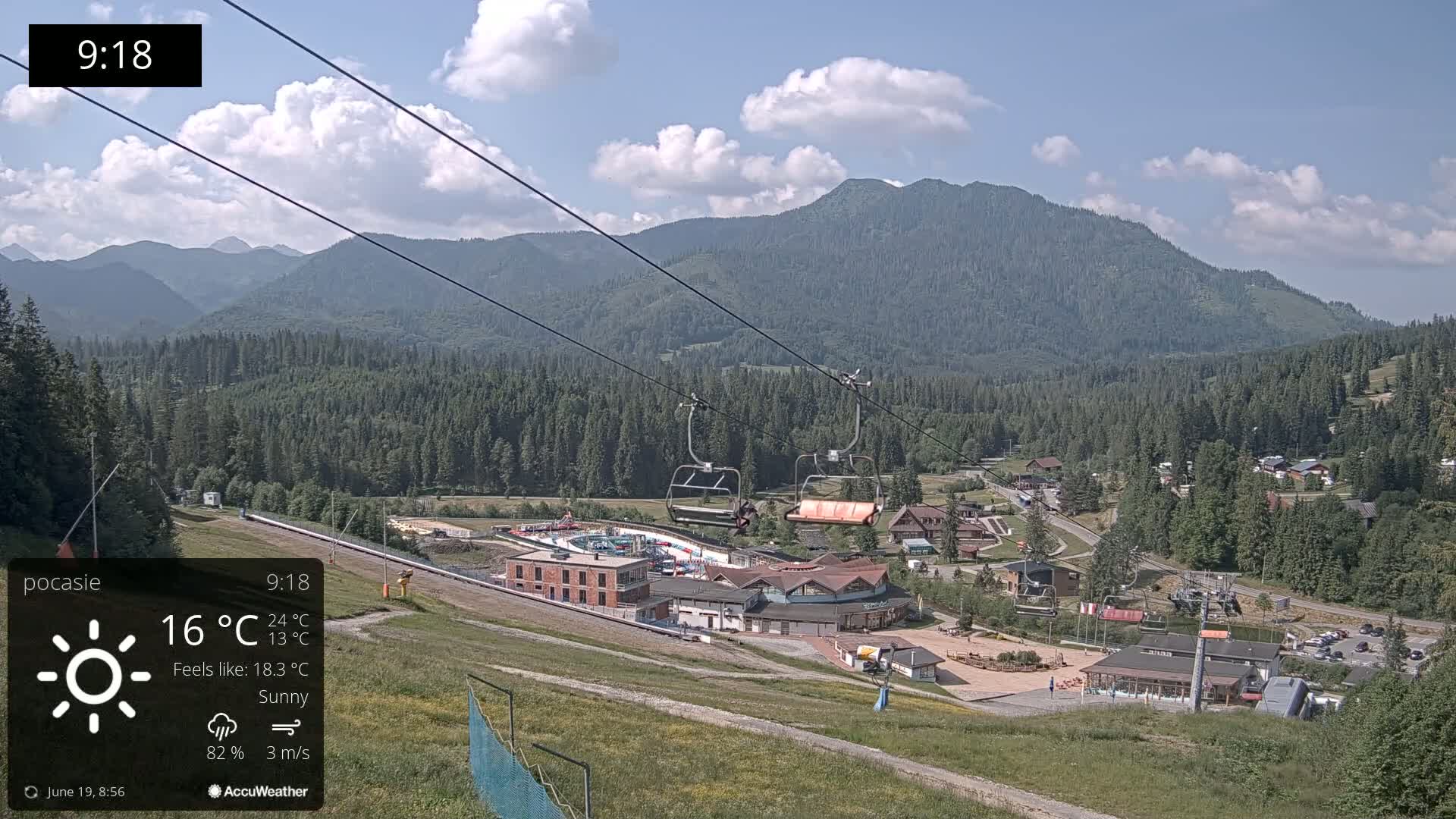 A sunny mountain vista shows a ski resort with a chairlift and several buildings, under partly cloudy skies.