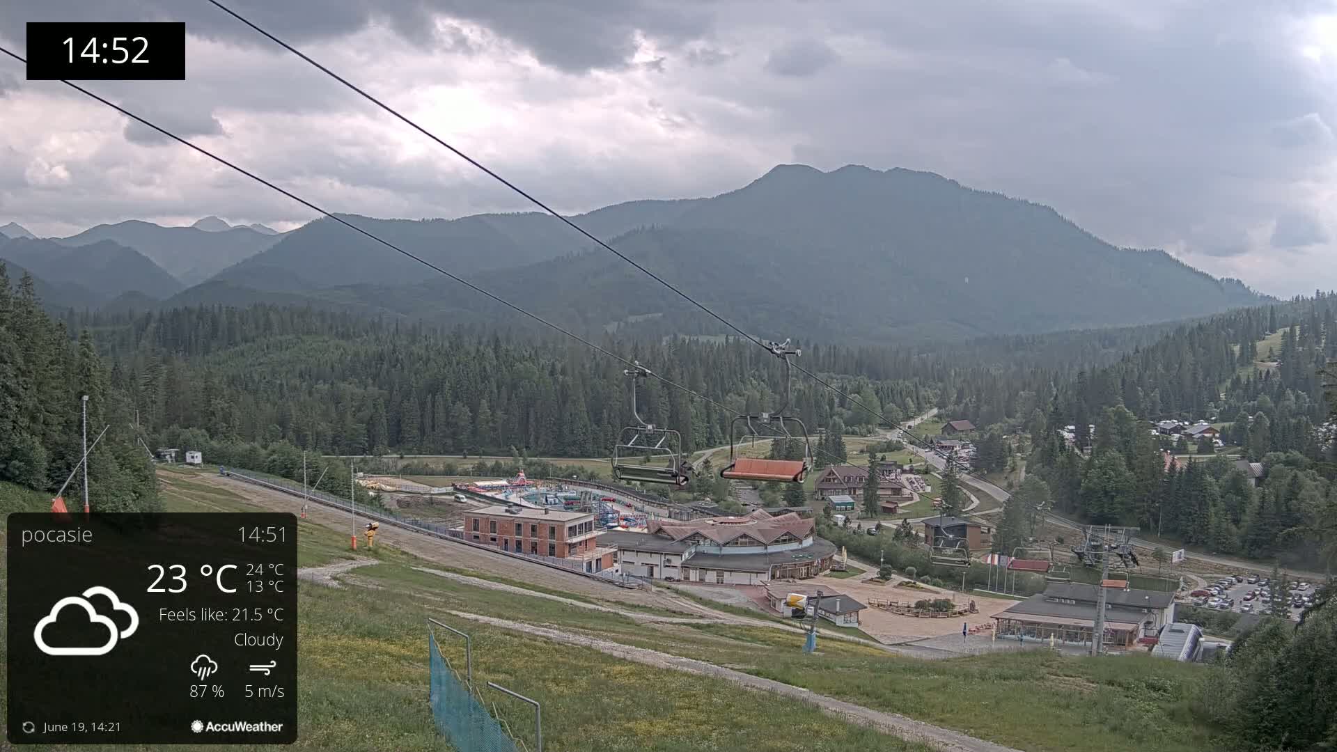 A chairlift ascends a mountainside overlooking a resort village under a cloudy sky.