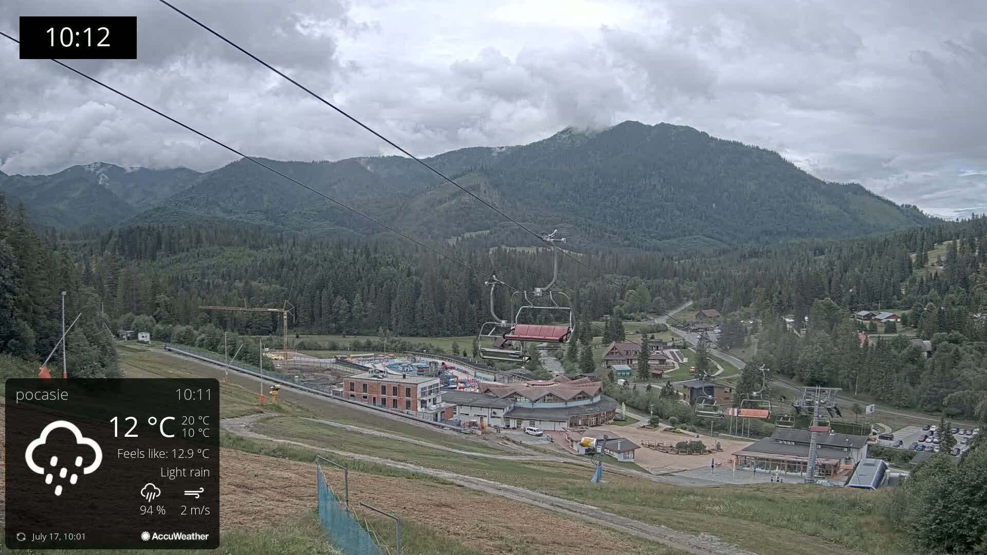 A chairlift ascends a mountain range under a cloudy sky with light rain.