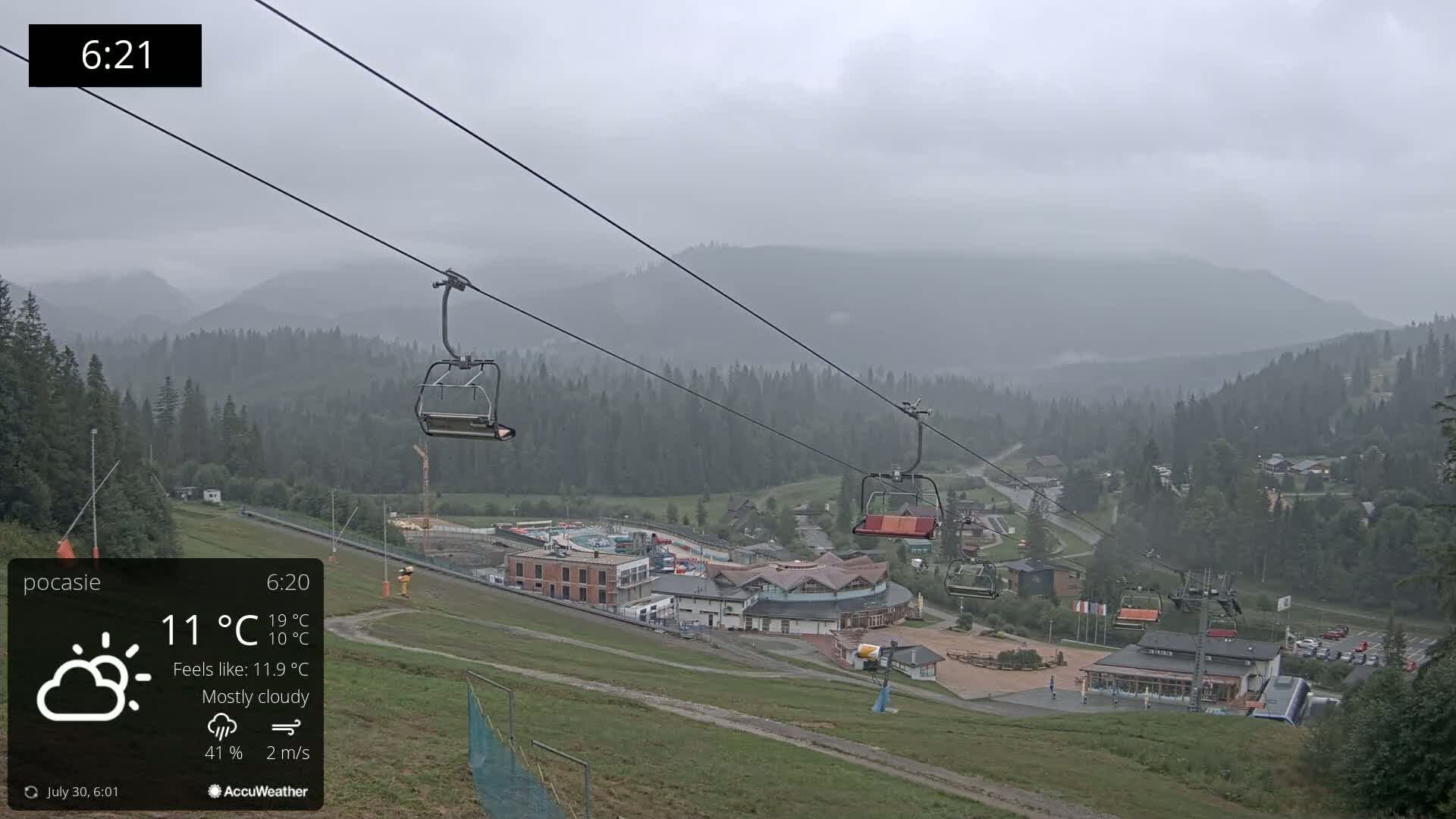 A chairlift ascends a mountain range under a cloudy sky with light rain.