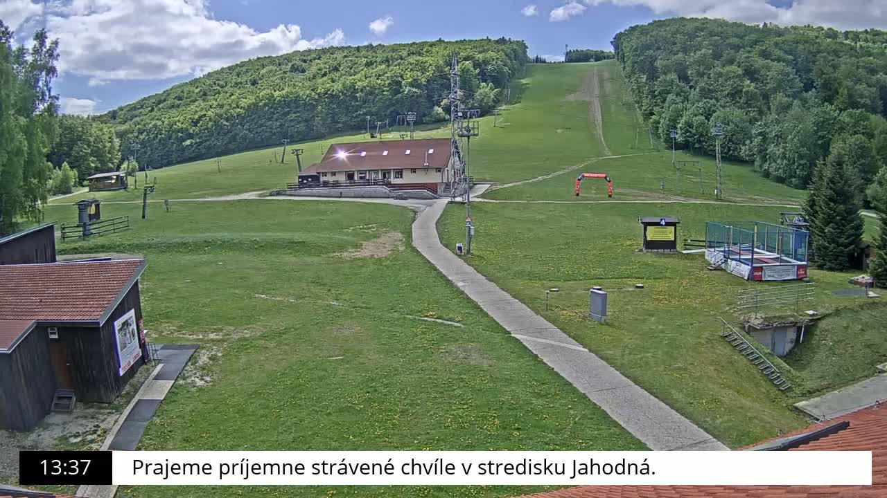 A ski slope with a building and other structures is visible on a sunny day with partly cloudy skies.