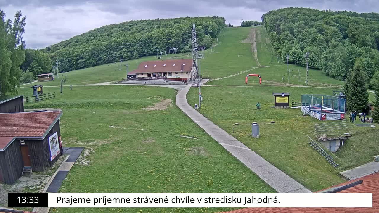 A grassy hill with a building, ski lift infrastructure, and a small trampoline park is visible under a cloudy sky.