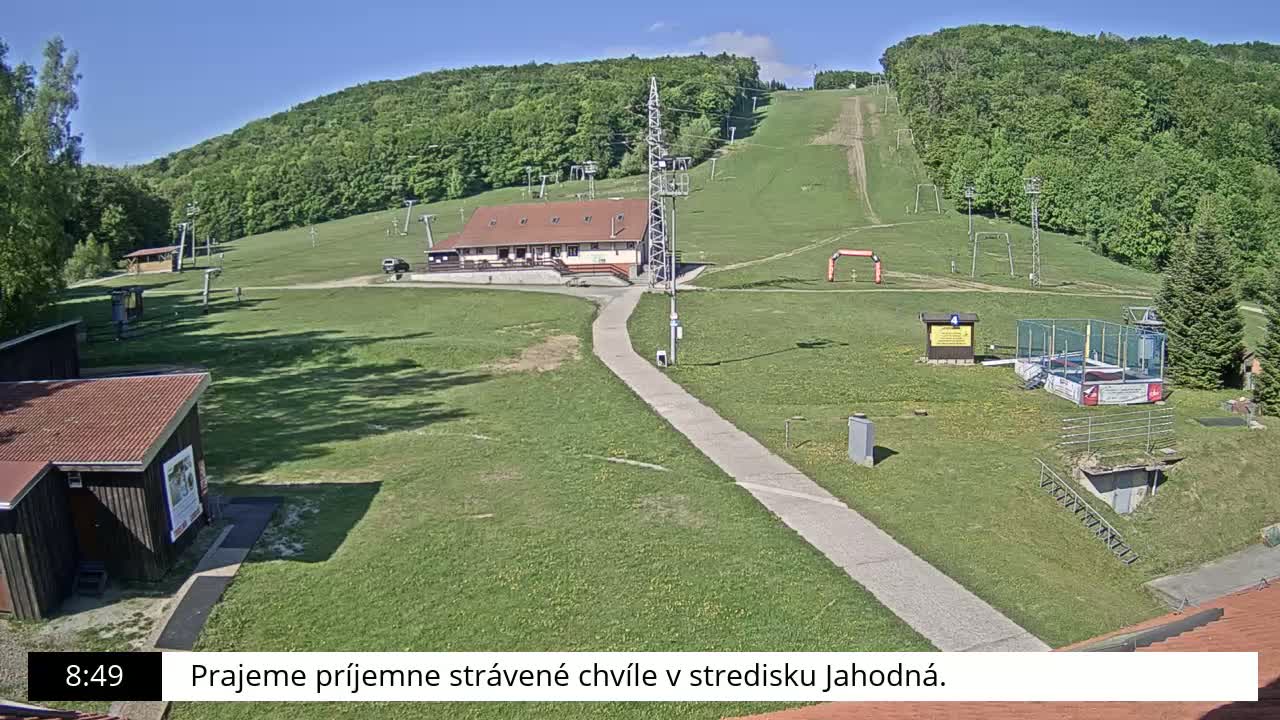 A ski resort with a main building, ski lifts, and grassy areas is visible under a clear, sunny sky.