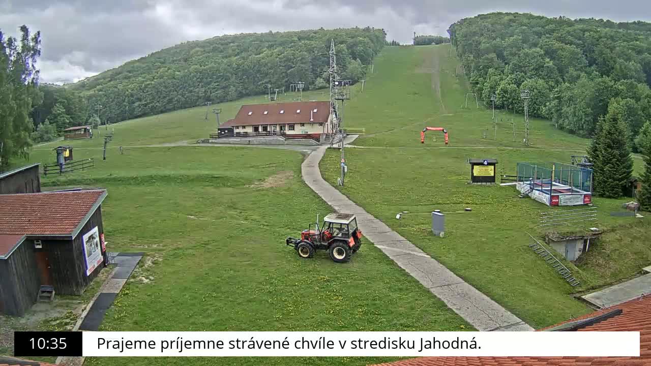 A grassy hillside with a ski lift, a small building, a tractor, and overcast skies.