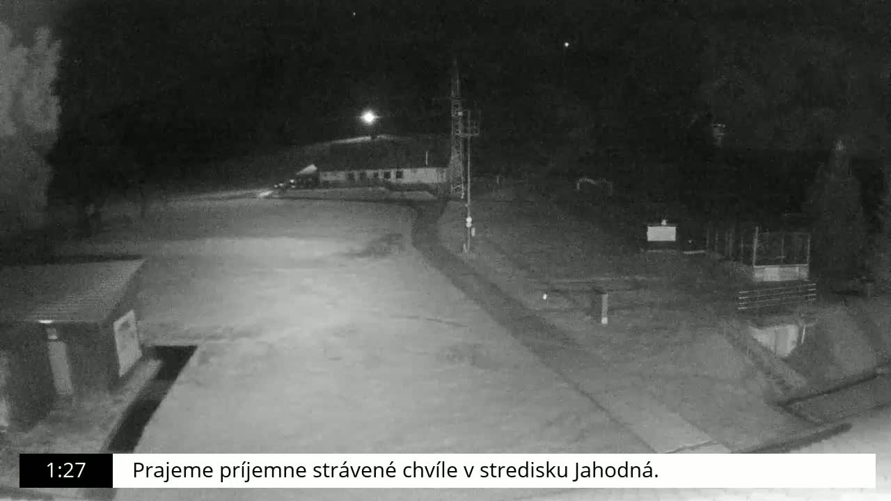 A nighttime, low-light view of an empty parking lot and a building, possibly a resort or ski lodge.